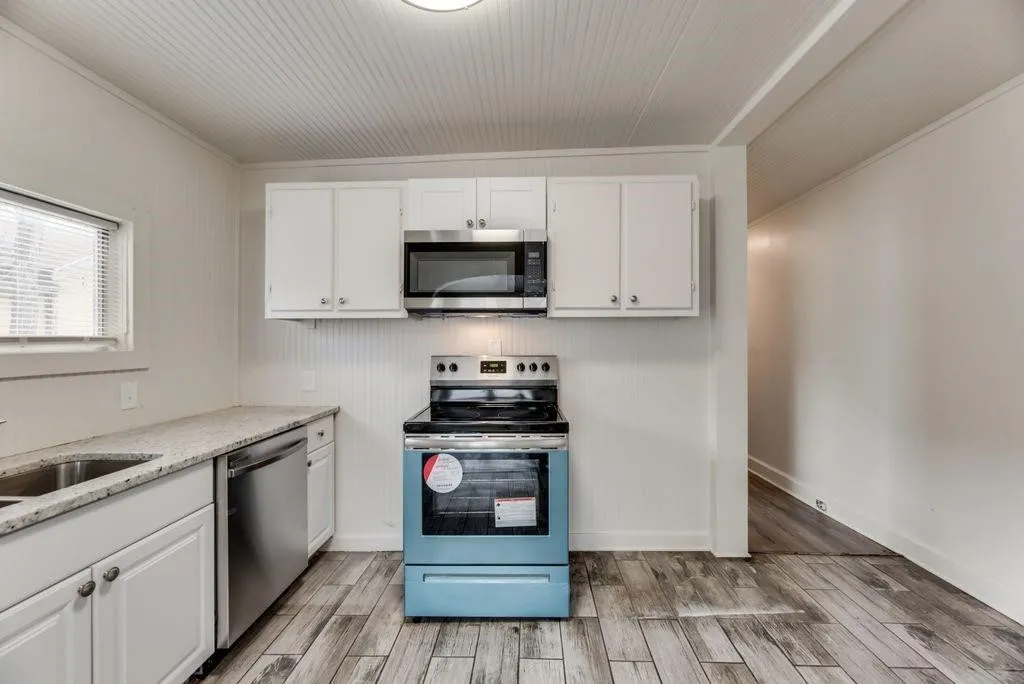 Kitchen featuring wood-finish flooring, white cabinetry, integrated stainless steel dishwasher, stainless steel microwave, and light-toned countertops