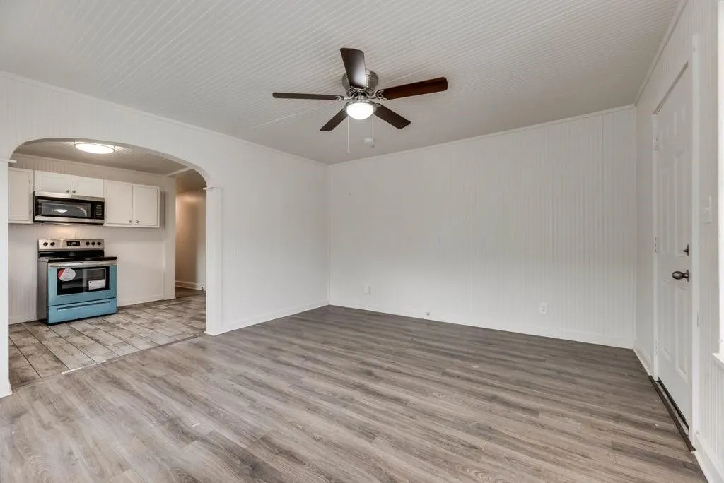 Wood-finish flooring, beadboard wall paneling, beadboard ceiling, ceiling fan with light fixture, and arched doorway