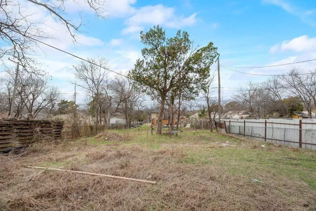 Expansive lot featuring a mix of natural ground cover and mature trees, bordered by a wood-slat fence and a chain-link fence