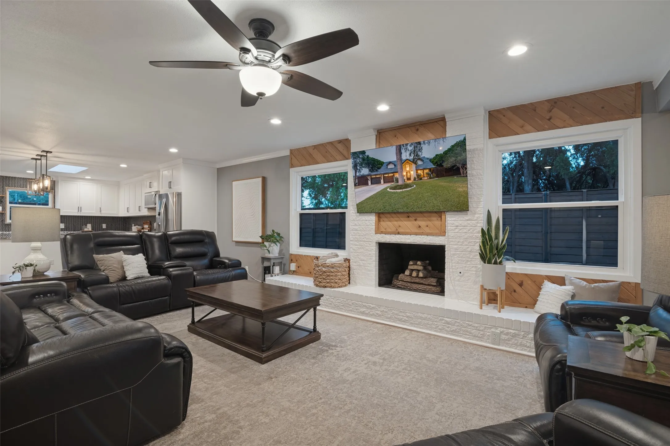 Feauturing a painted brick fireplace with custom wood accent trim and raised hearth, the spacious living room includes accent lighting, an upgraded ceiling fan, and a tree-lined view of the large, fenced, side yard.