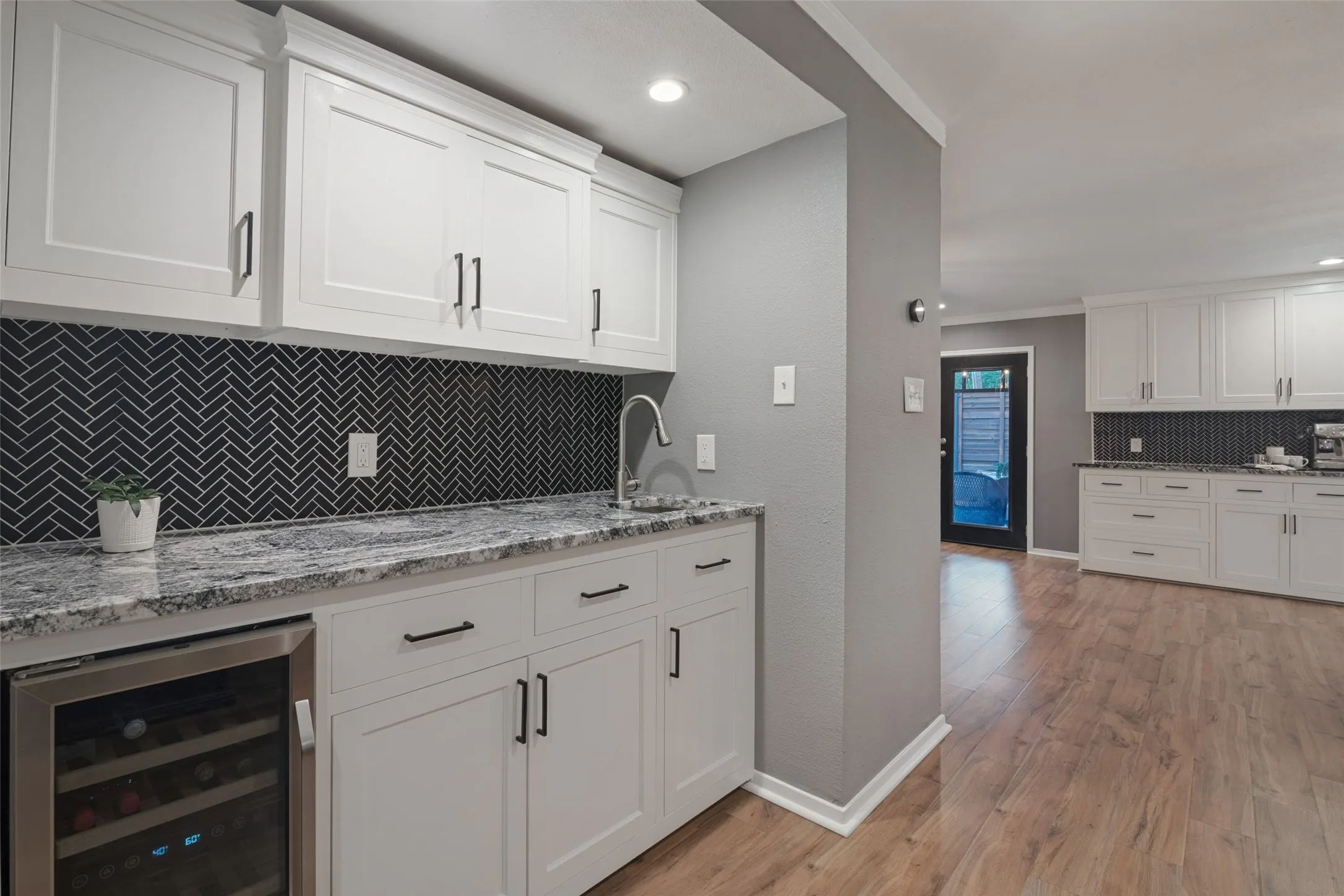 This handy wet bar provides additional storage cabinets, a built-in beverage fridge, and is accented with the same stunning granite and chevron style tile backsplash as the kitchen.