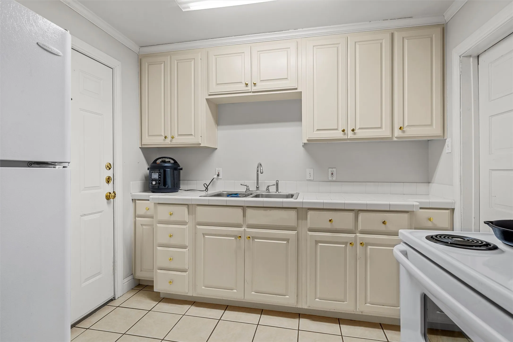 Kitchen featuring white cabinetry with gold-toned hardware, a stainless steel double basin sink, and a white tile backsplash