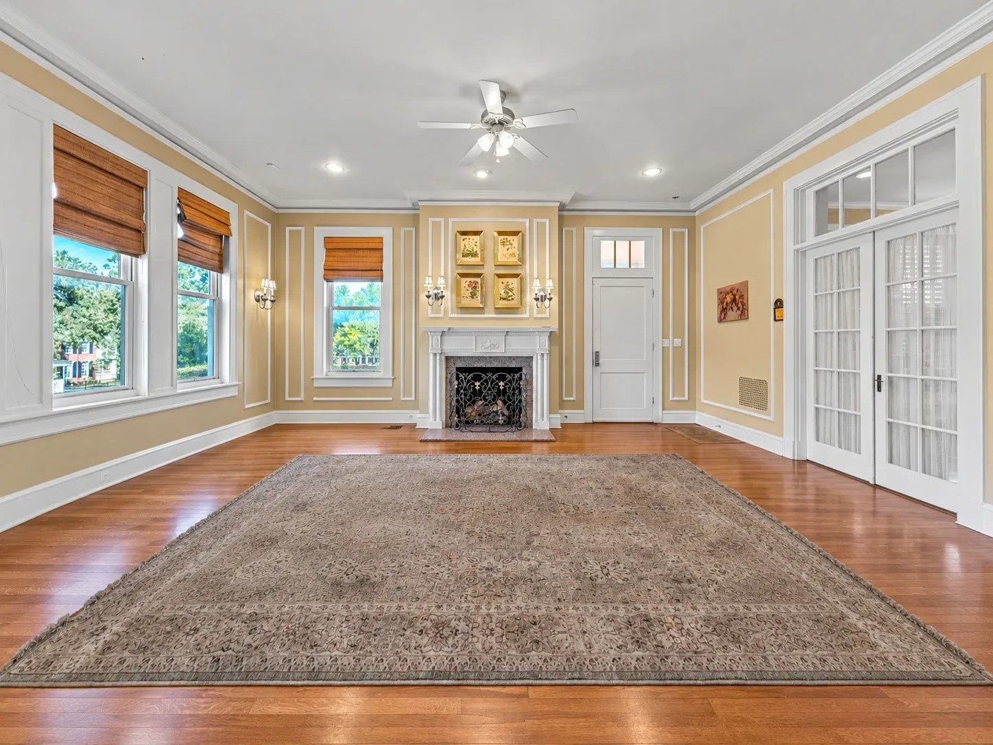 Hardwood flooring, decorative wall molding, fireplace with mantel, ceiling fan, and French doors
