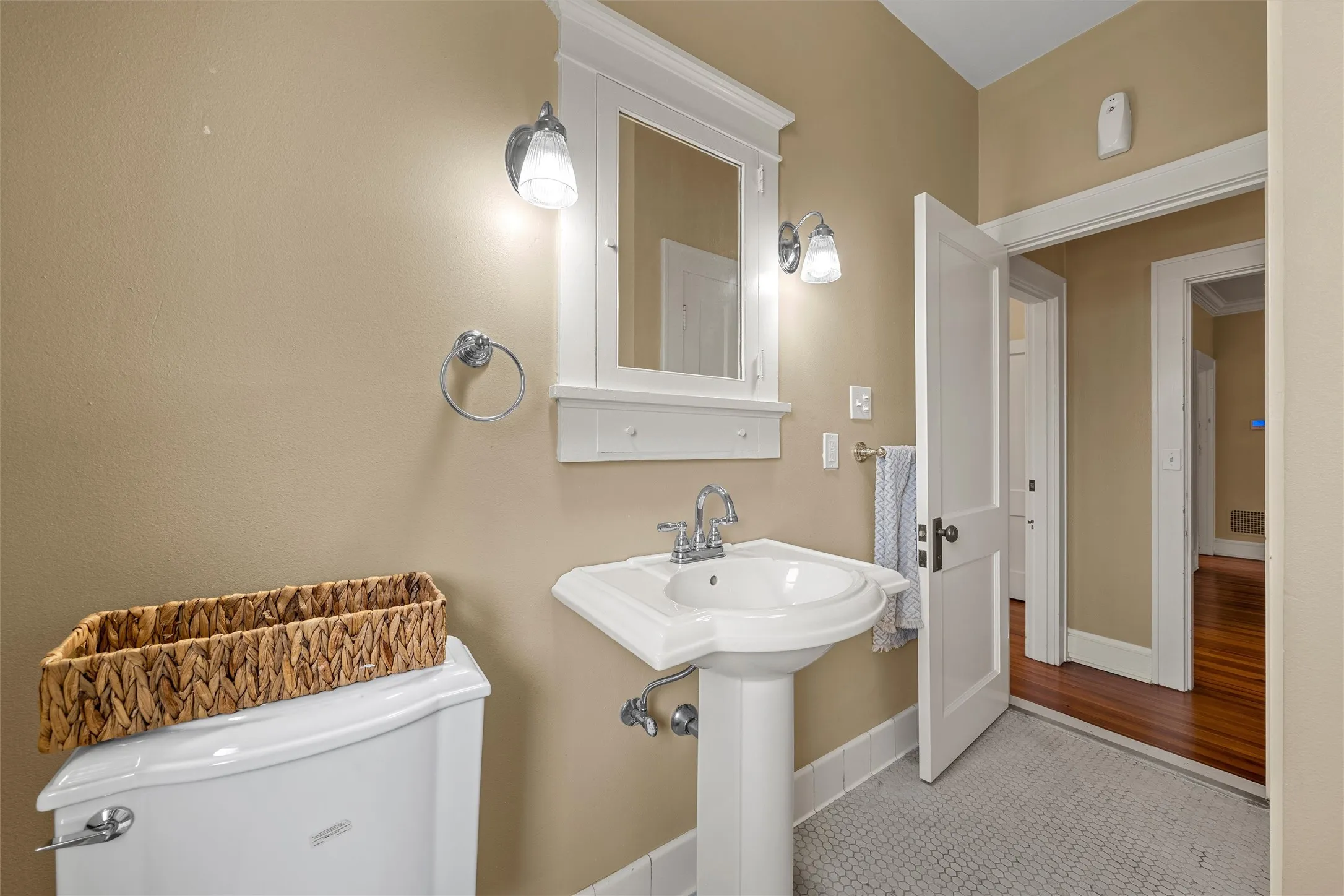 Pedestal sink with chrome faucet, wall-mounted mirror with integrated shelving, and dual sconce lighting
