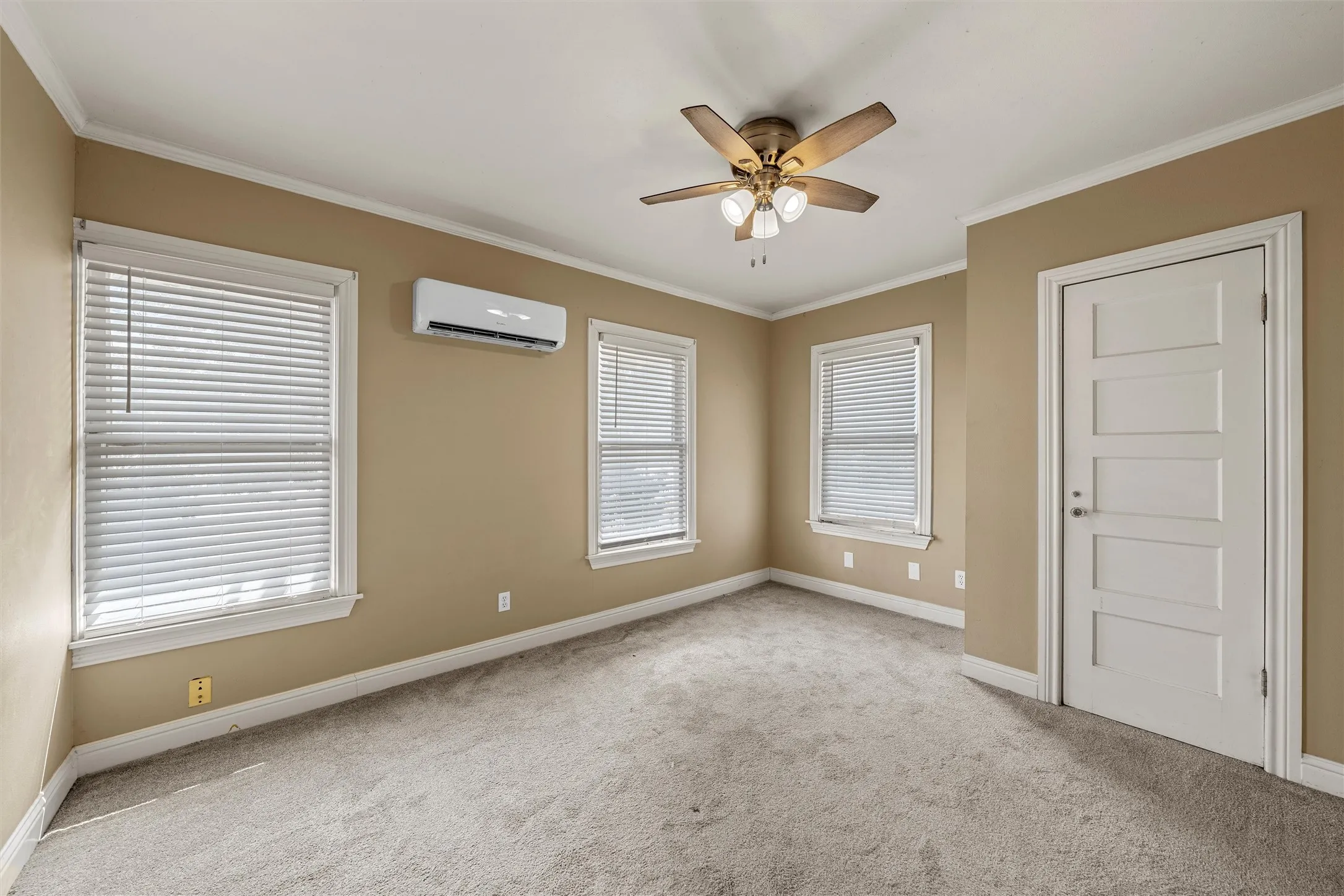 Plush carpeting, ceiling fan, two windows with blinds, mini-split air conditioning unit, and a five-panel interior door