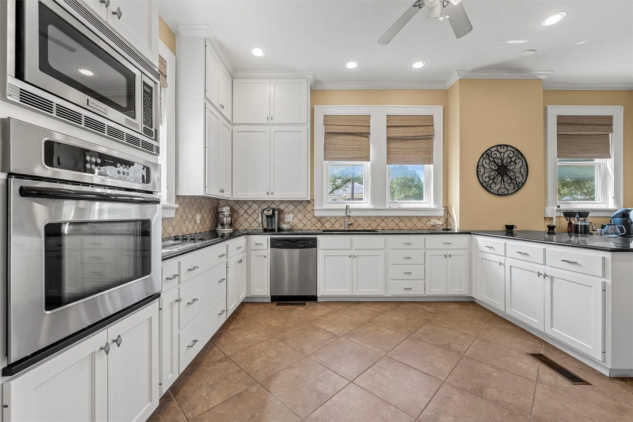 Kitchen featuring white cabinetry, stainless steel appliances, dark countertops, a patterned tile backsplash, and tile flooring