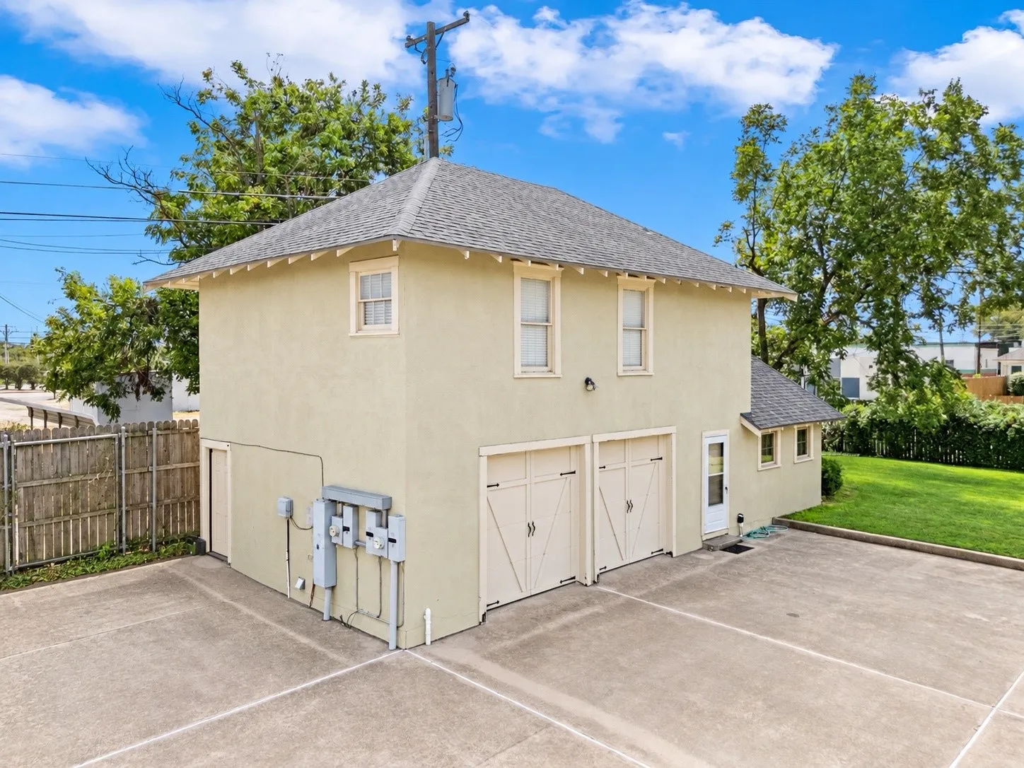 Two-story structure with stucco exterior, two garage bays, multiple windows, and a paved parking area