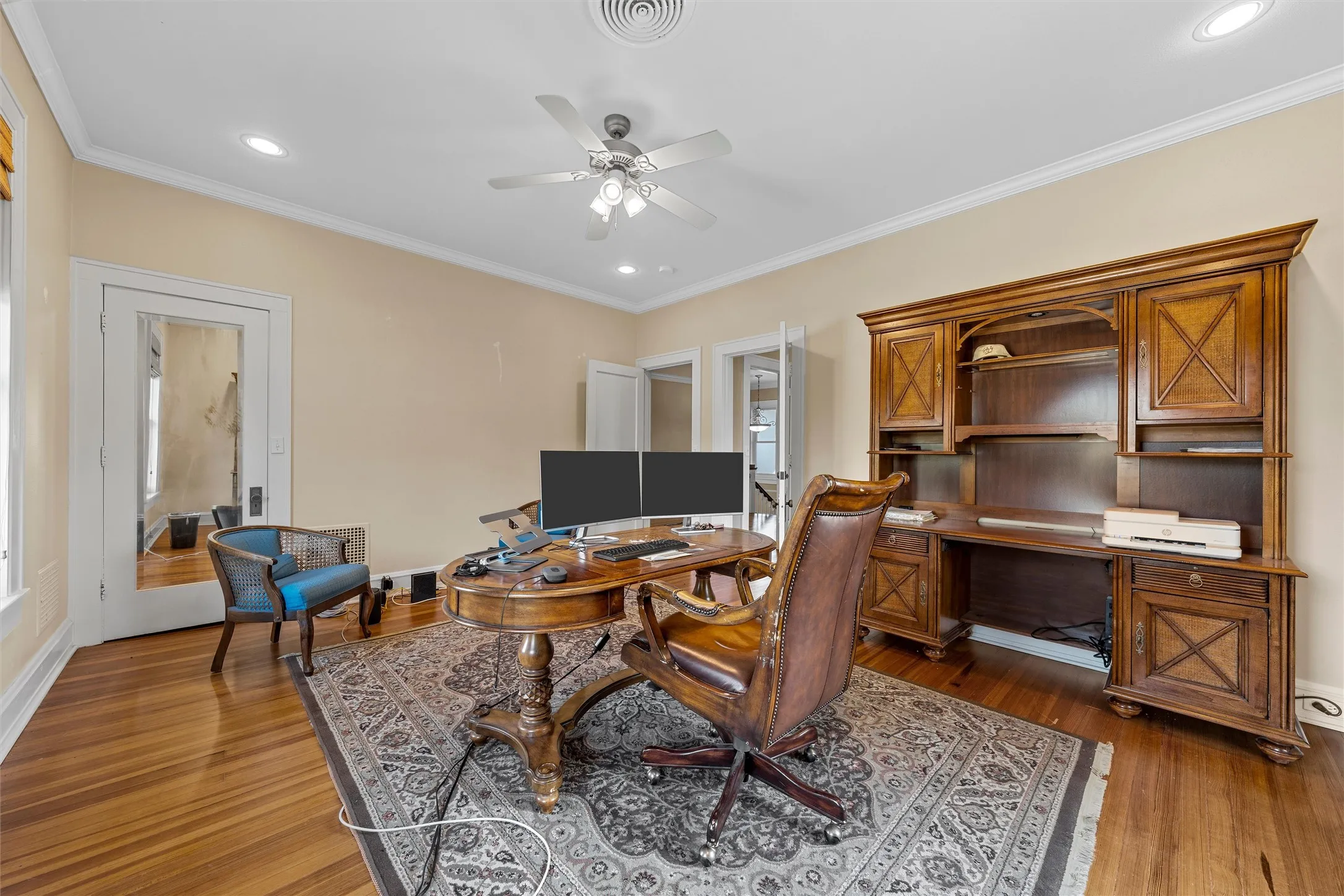 Wood-finish flooring, recessed lighting, crown molding, ceiling fan, and built-in desk cabinetry