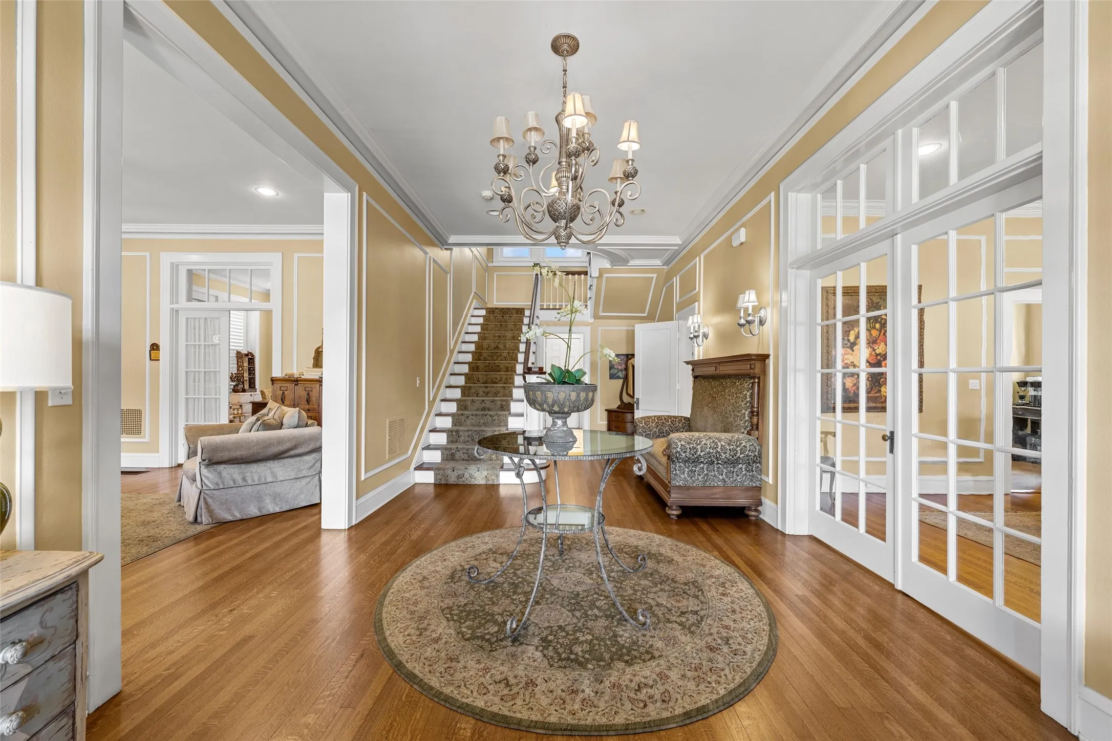 Hardwood flooring, an ornate chandelier, a staircase with a runner, and interior French doors