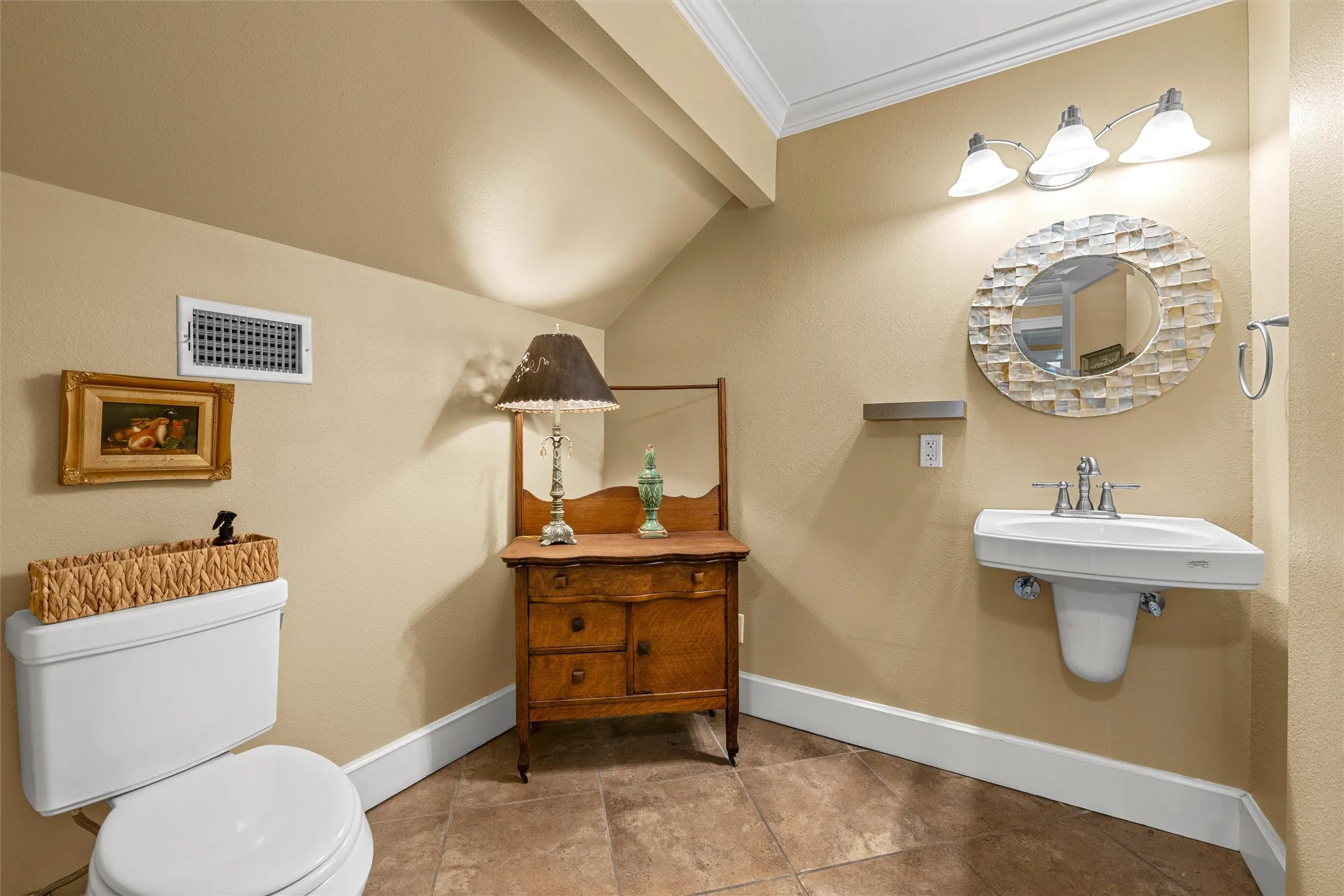 Wall-mounted sink with brushed nickel faucet, oval mirror with textured frame, three-light vanity fixture, crown molding, and tiled flooring
