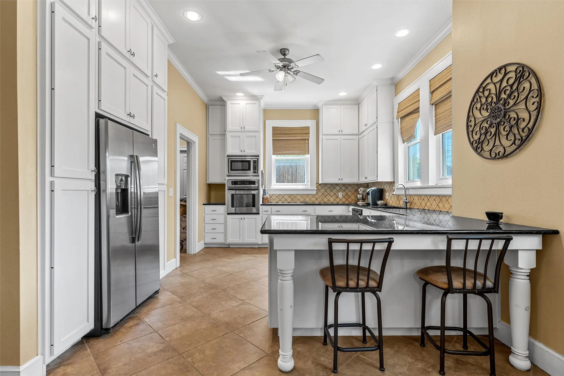 Spacious kitchen featuring white cabinetry, integrated stainless steel appliances, a large island with counter seating, neutral-toned tile flooring, and a decorative tile backsplash