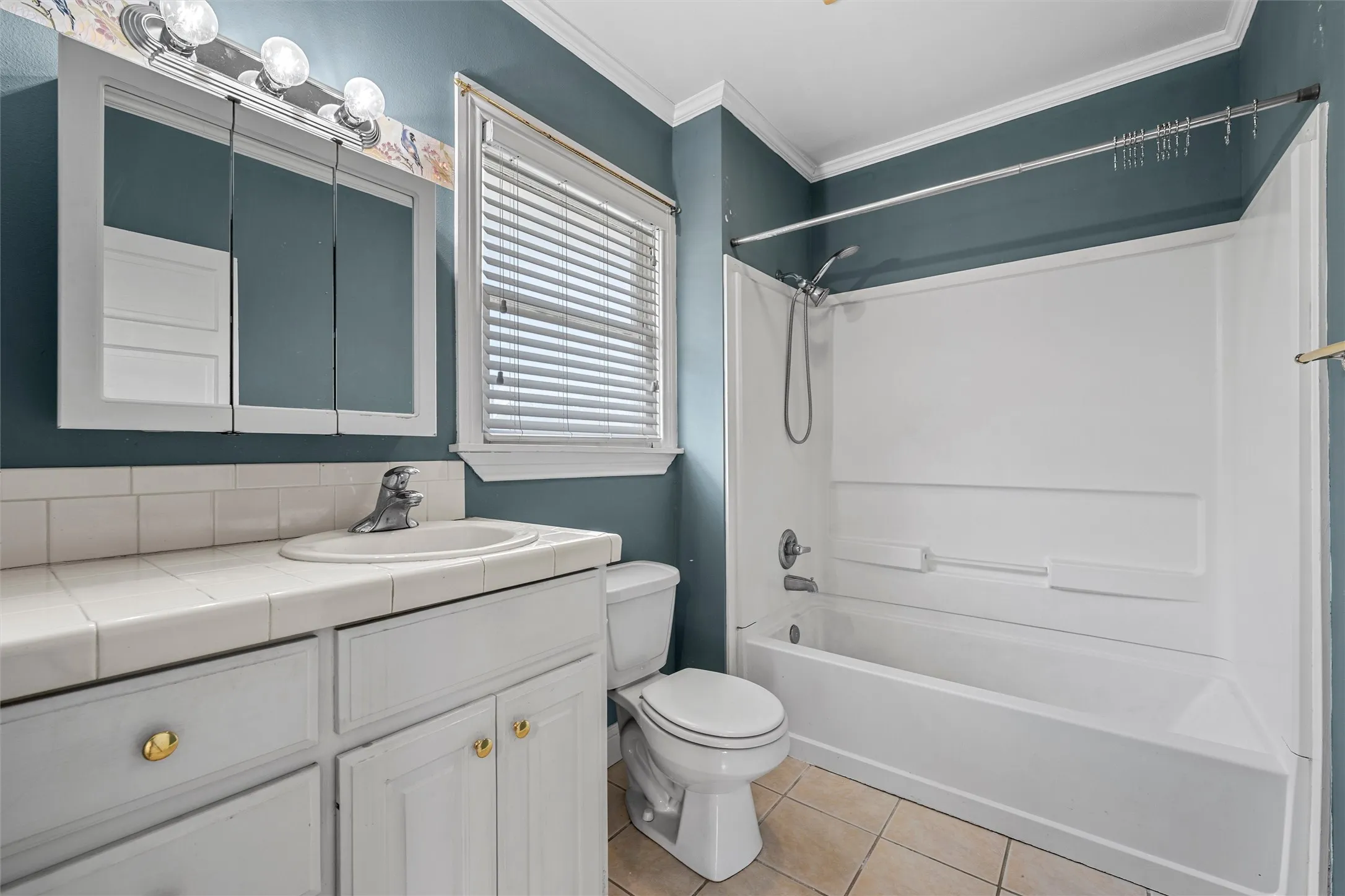 Vanity with white cabinetry and tiled countertop, recessed sink with chrome faucet, and a wall-mounted mirrored medicine cabinet