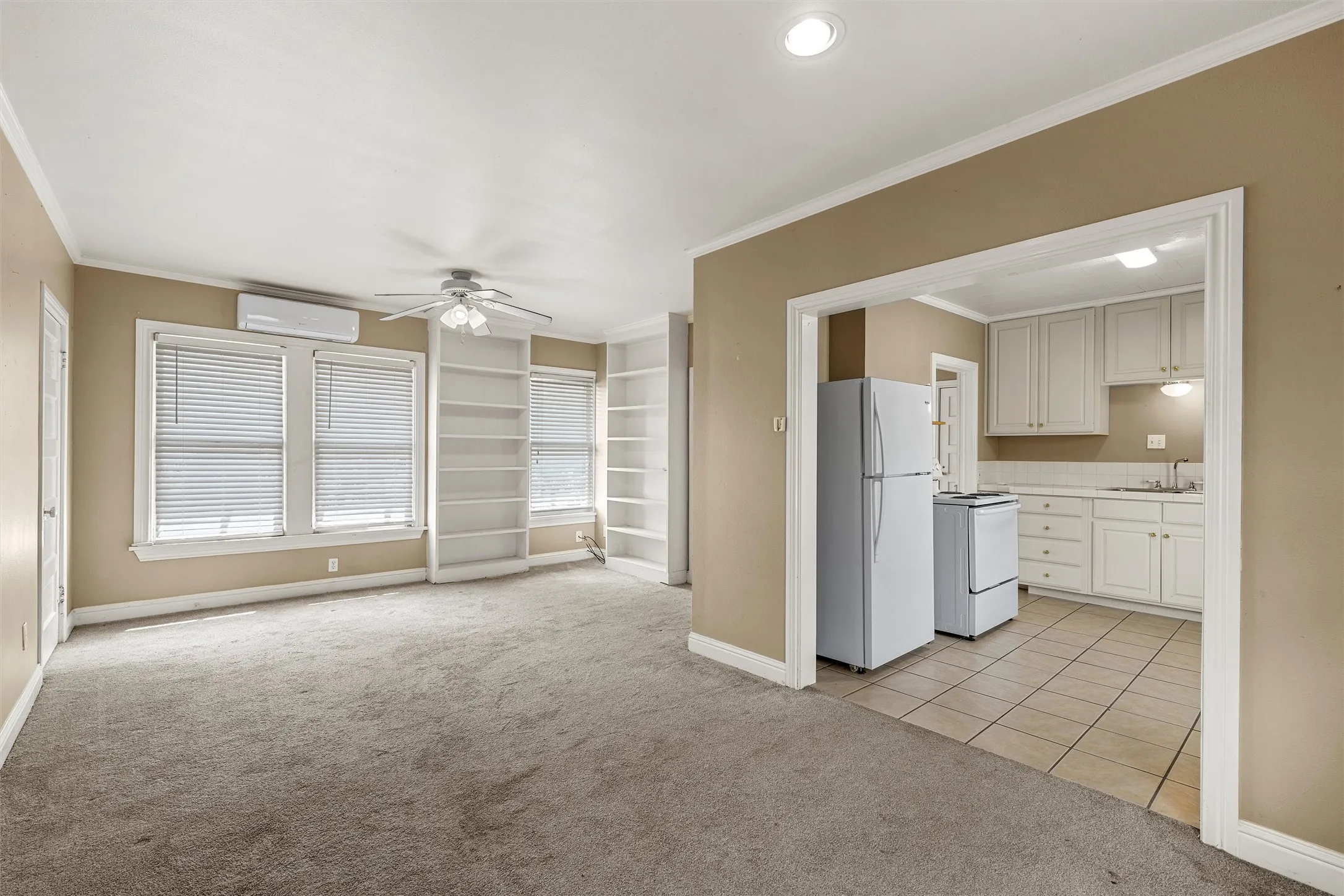 Carpeted living area with built-in shelving, ceiling fan, and window blinds
