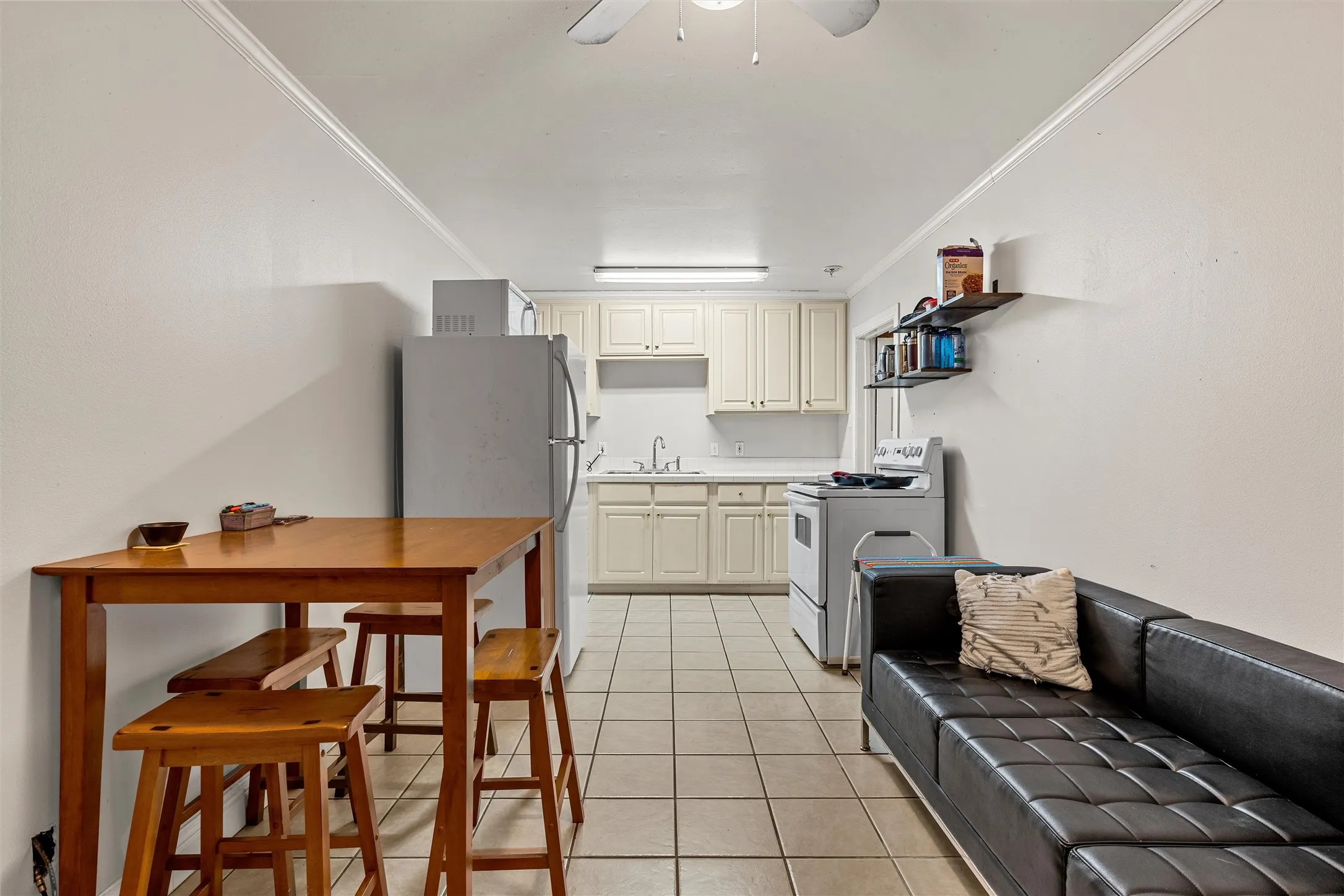 Compact kitchen area featuring cream-colored cabinetry, a white stove, and a stainless steel refrigerator