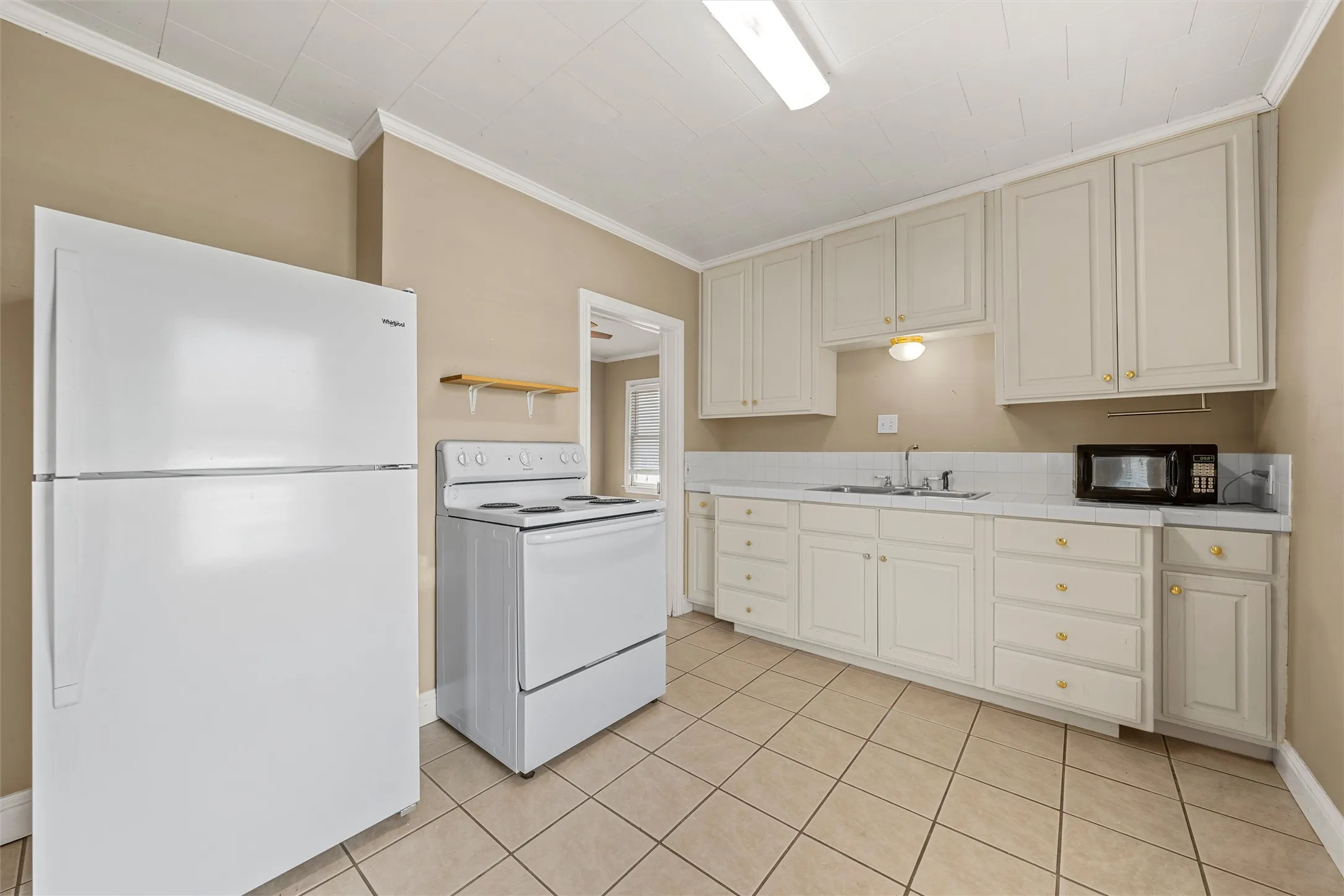Kitchen featuring white cabinetry with gold-toned hardware, white appliances, a tile backsplash, and tile flooring