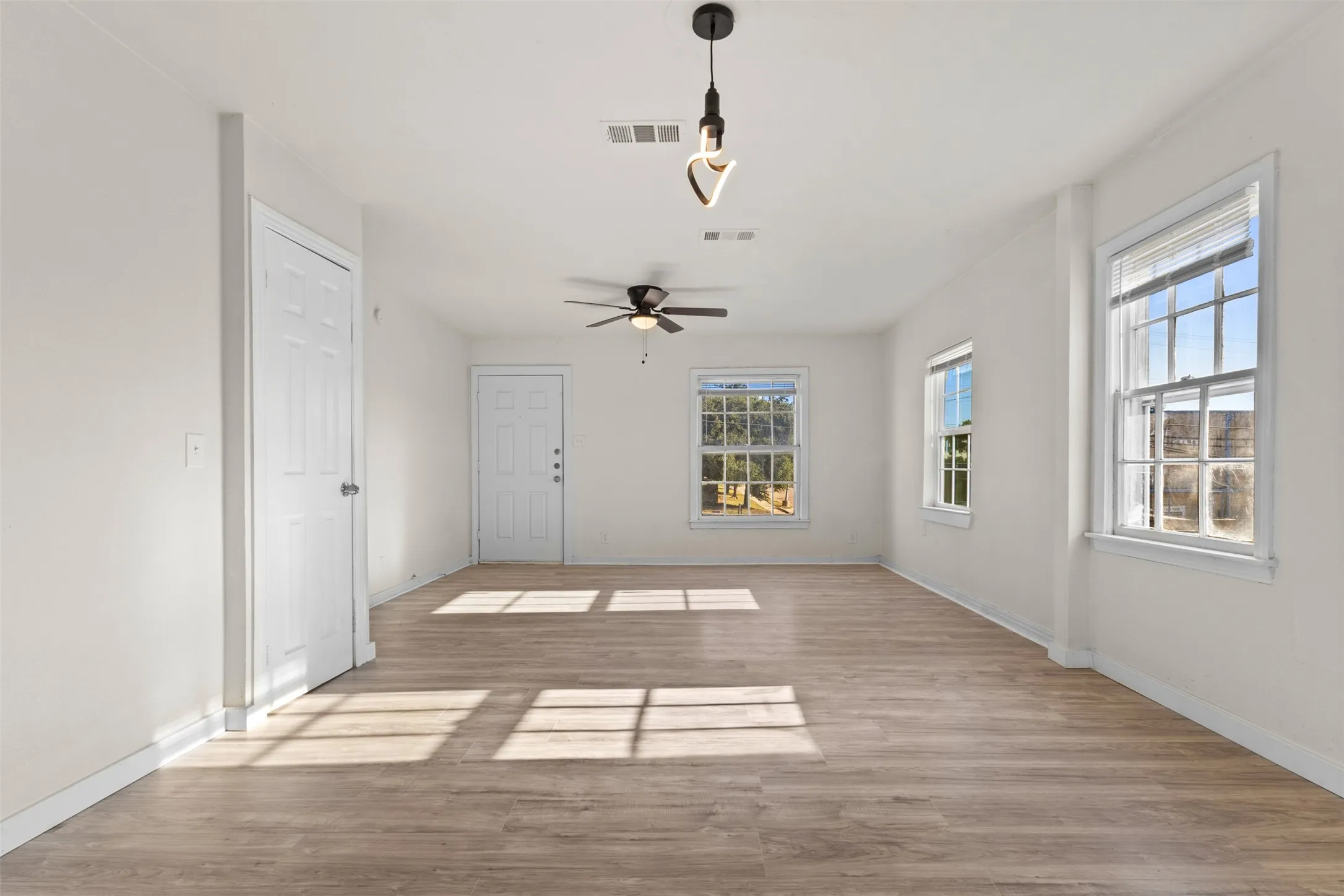 Open-concept living space featuring wood-finish flooring, multiple windows, a ceiling fan, and pendant lighting