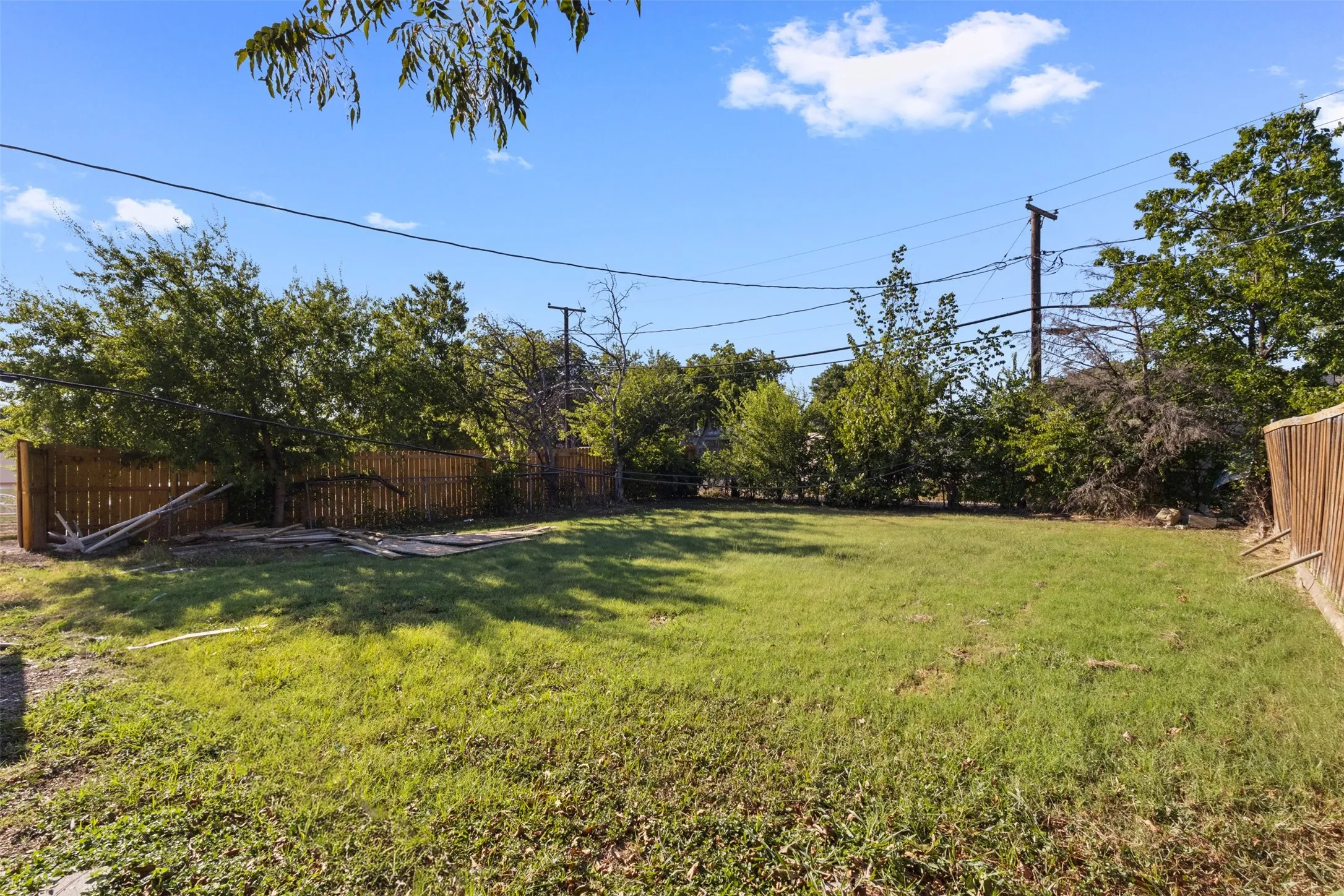 Expansive grassy yard with a wooden privacy fence, mature perimeter trees, and a clear sky backdrop