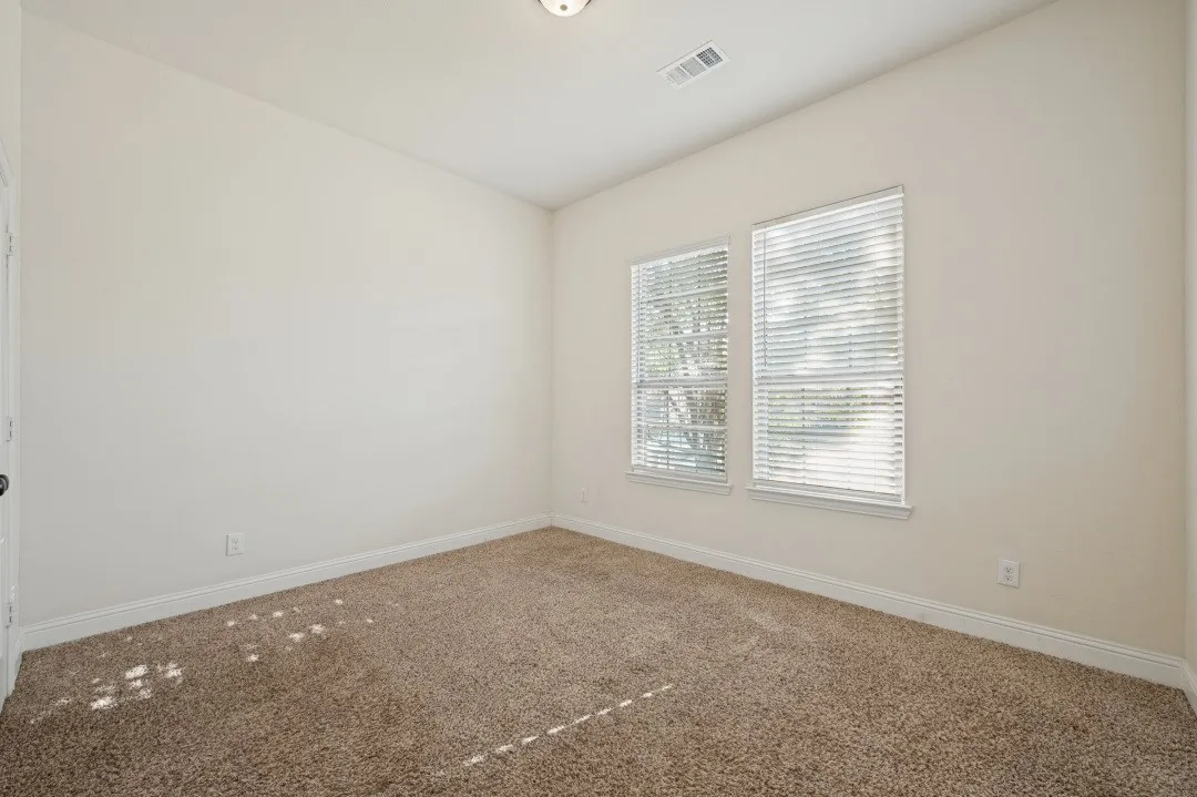 Carpeted flooring, white walls, two windows with blinds, and white trim throughout