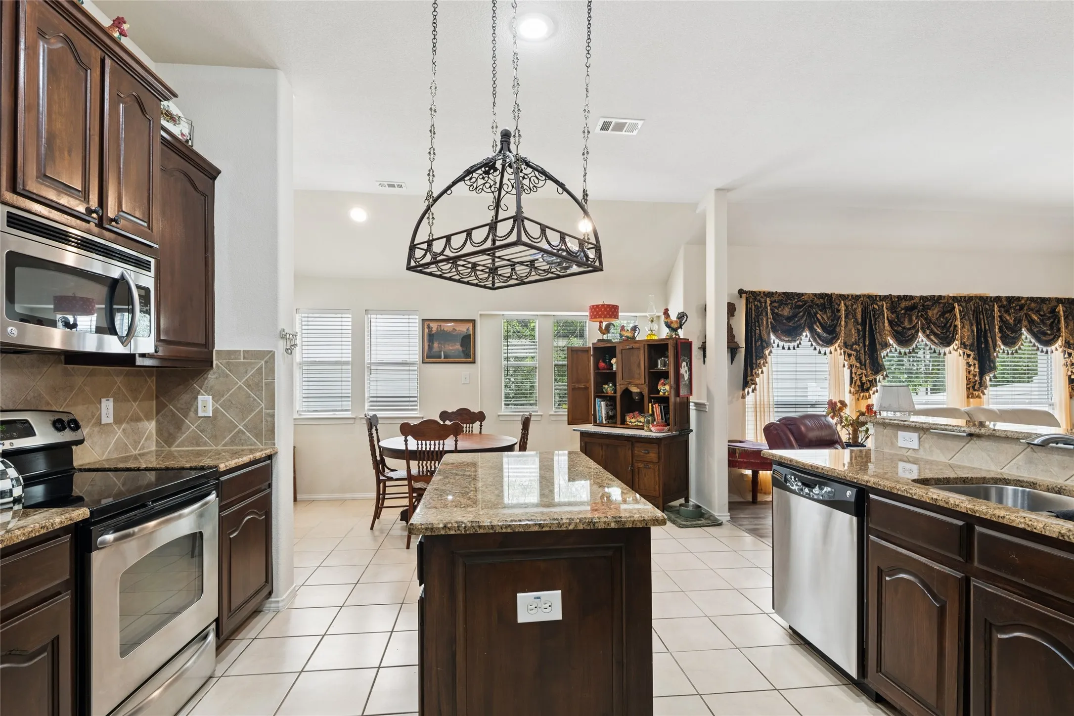 Kitchen featuring dark wood cabinetry, stainless steel appliances, granite countertops, and tile flooring