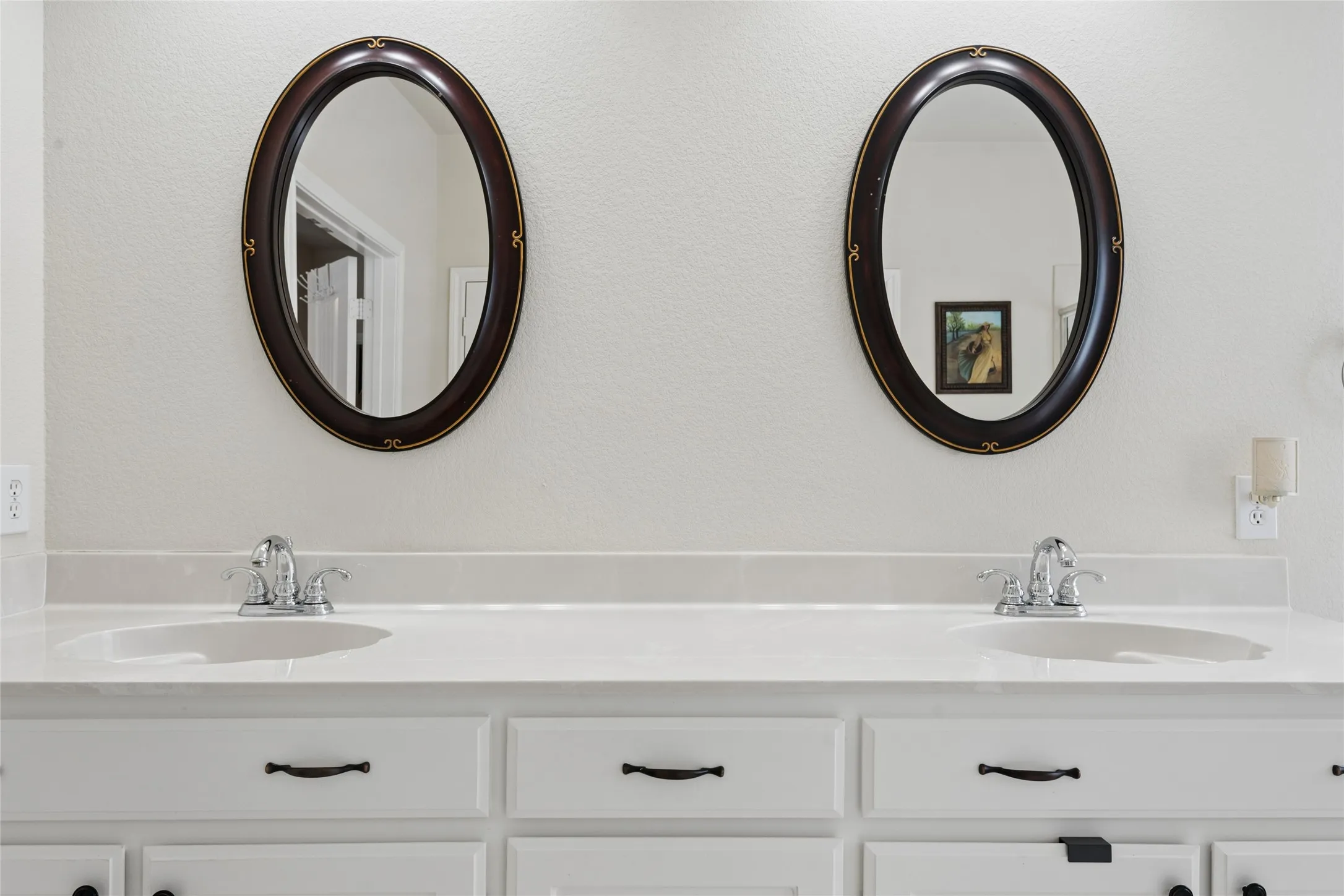 Dual oval mirrors with dark wood frames, double undermount sinks, and a white countertop
