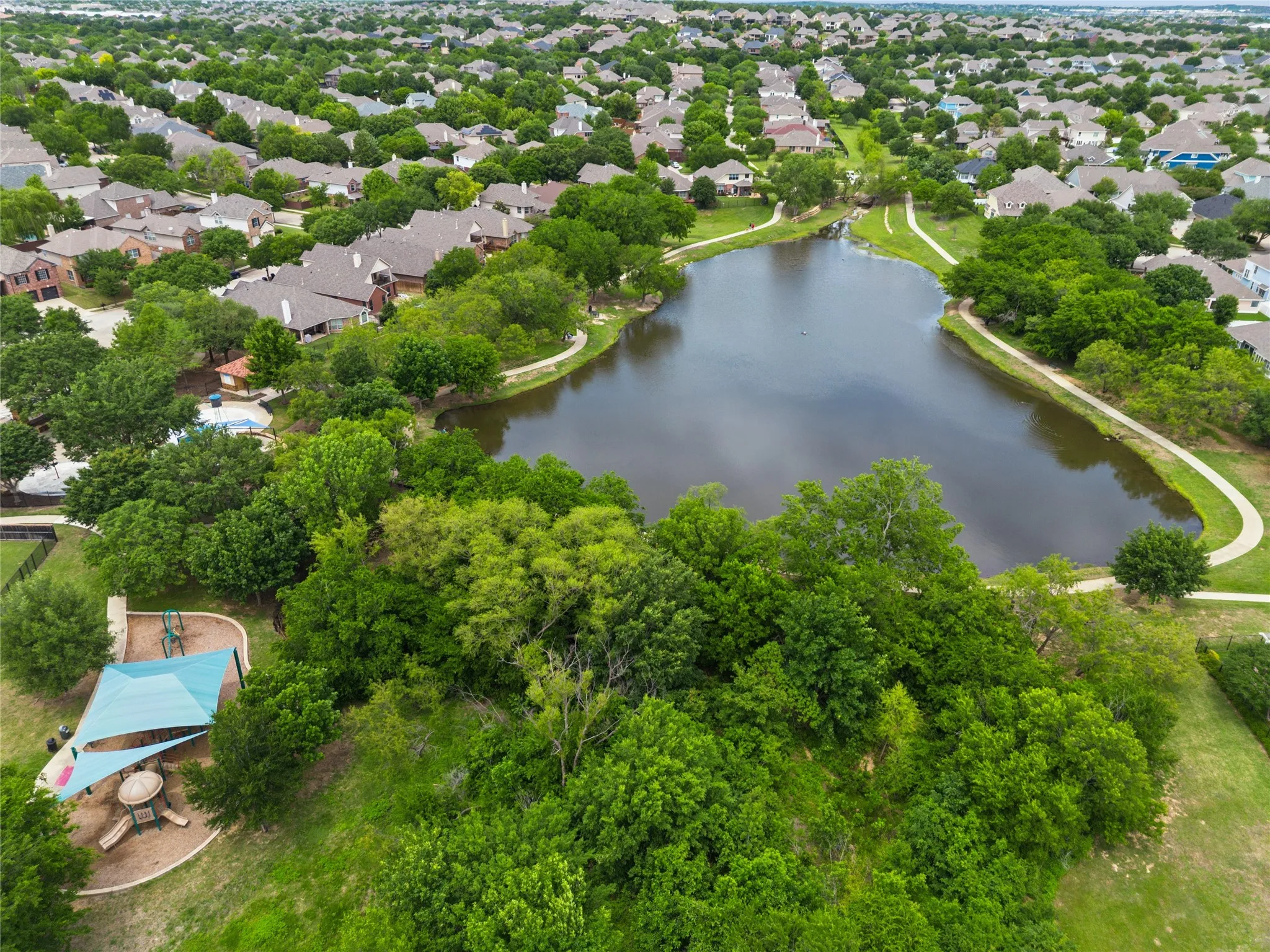 Aerial perspective showcasing a residential area with a prominent central lake, surrounding mature trees, and paved walking paths