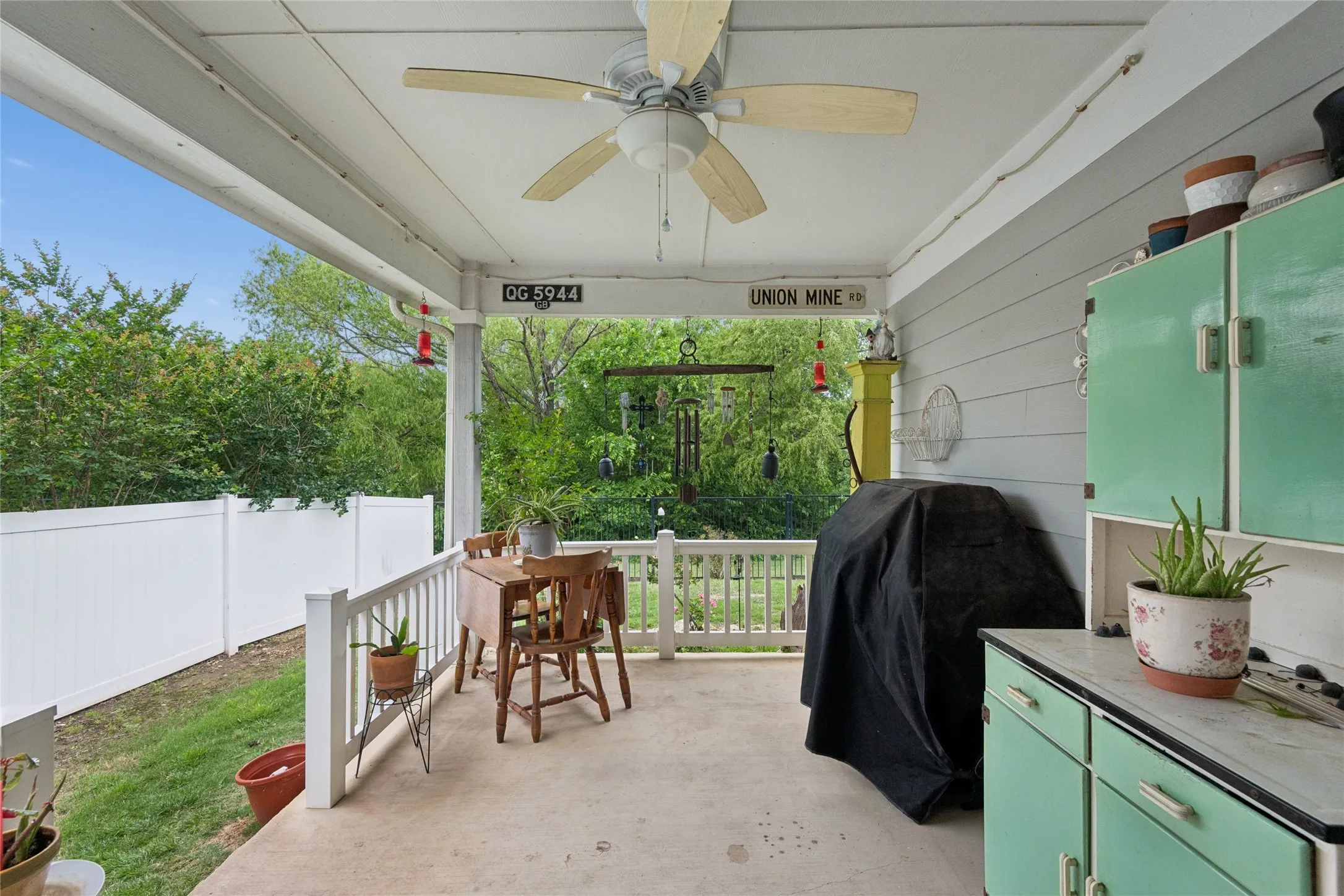 Covered porch with a ceiling fan, white vinyl fence, and built-in green cabinets