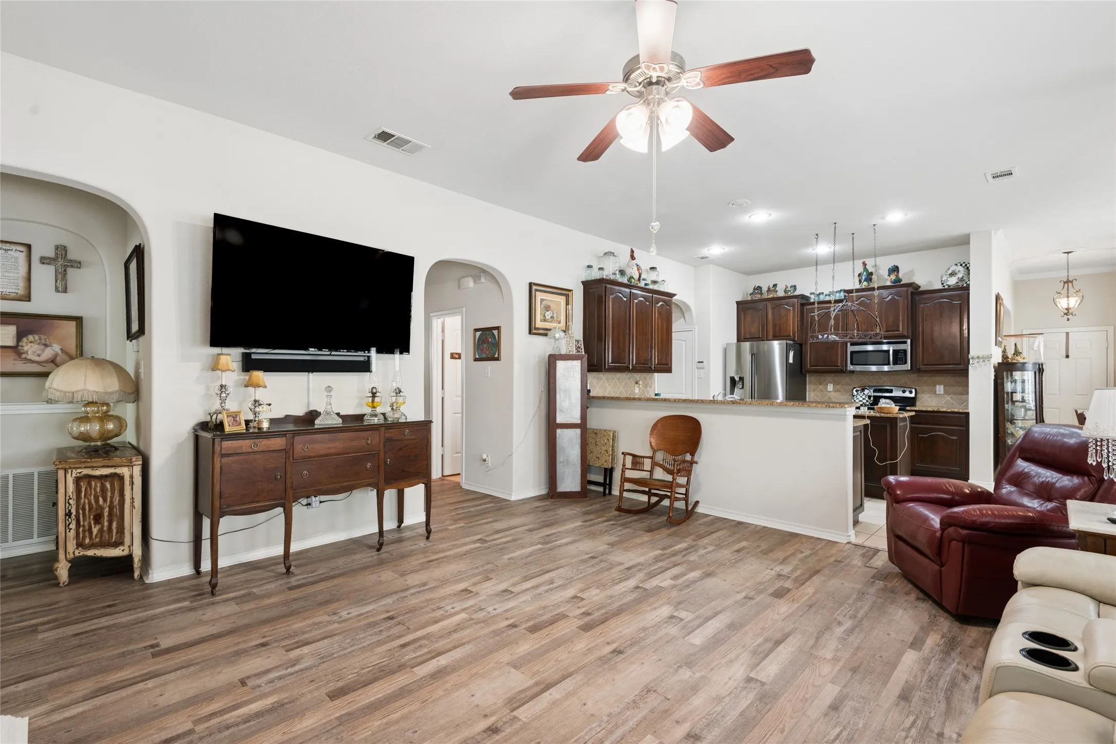 Open-concept living area with wood-finish flooring, a ceiling fan, and arched doorways