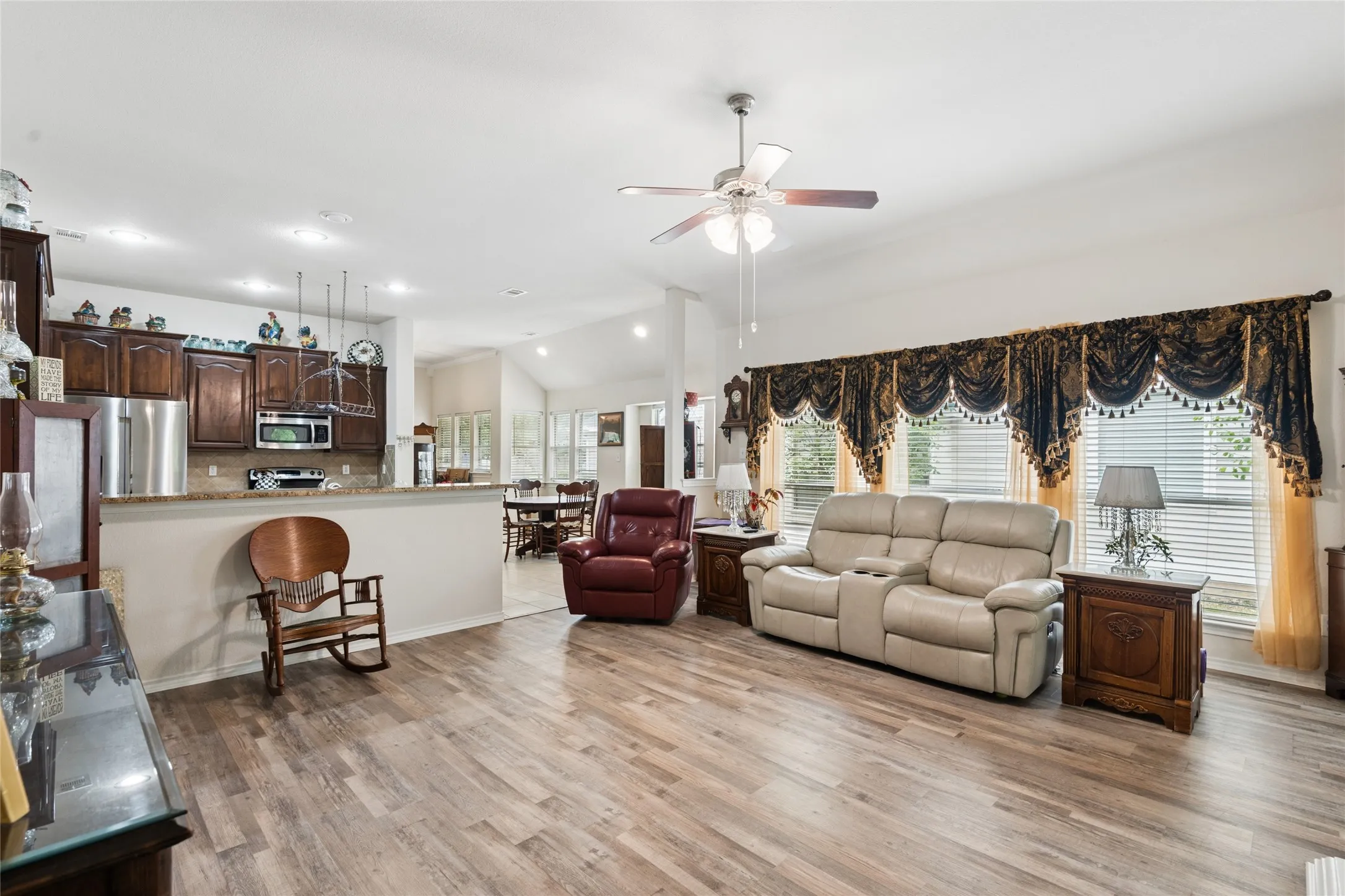 Wood-finish flooring throughout, vaulted ceiling, ceiling fan, and multiple windows with blinds