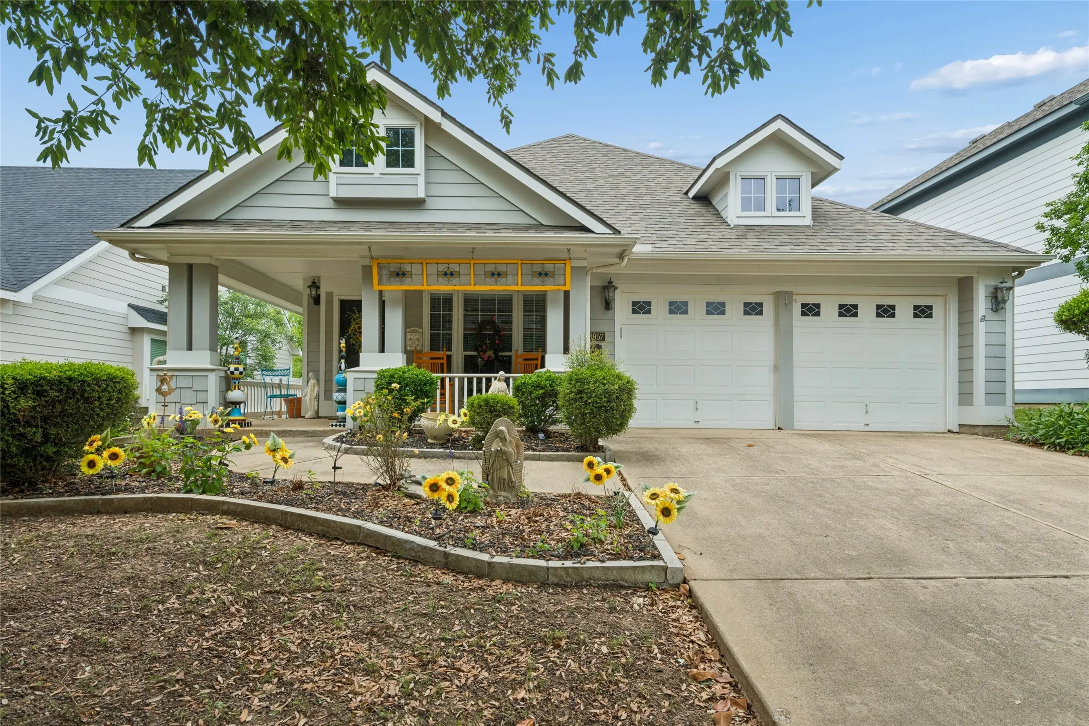 Gabled roofline with dormer windows, covered front porch, two-car garage, concrete driveway, and established front landscaping