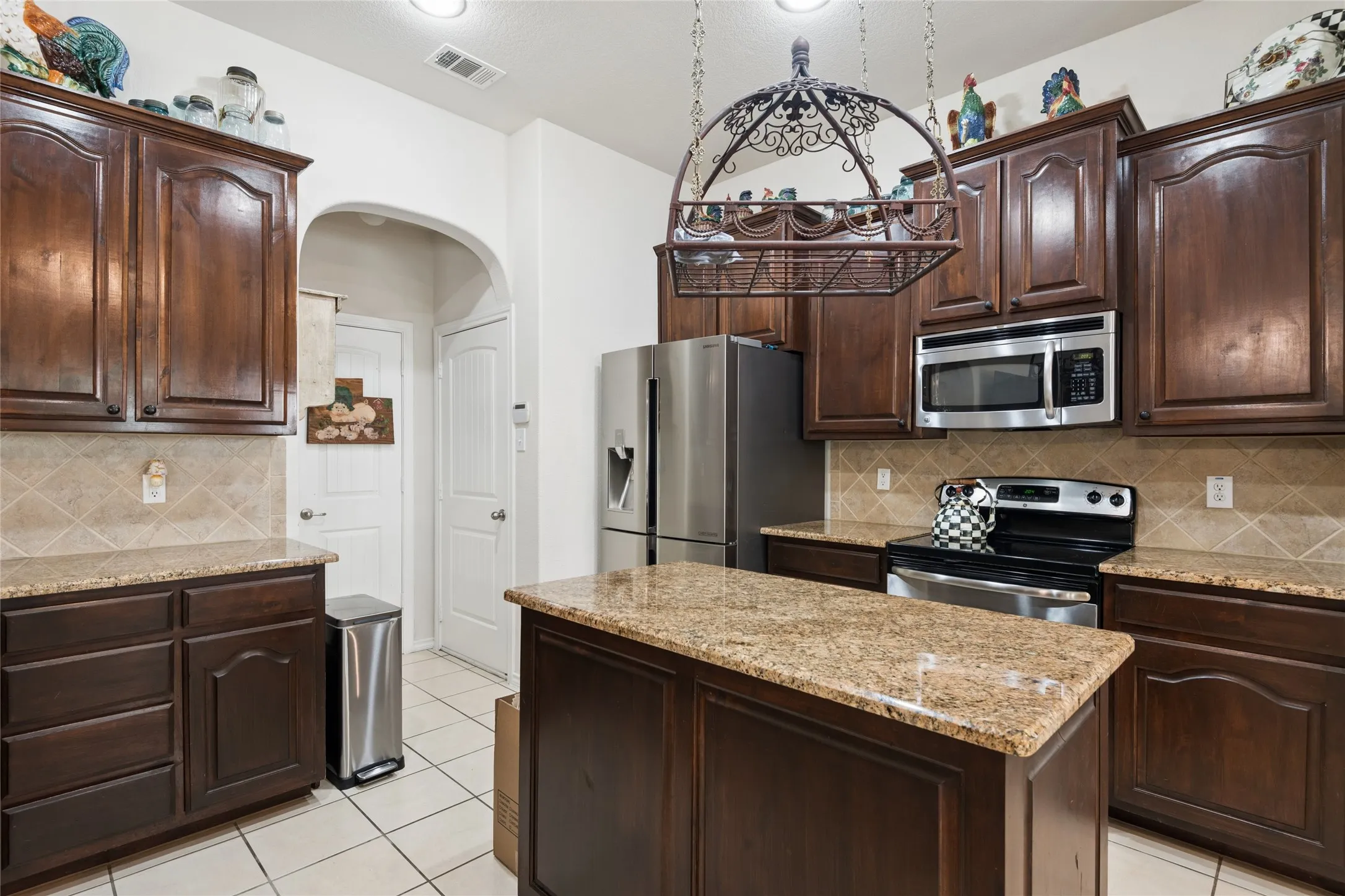 Kitchen featuring dark wood cabinetry, granite countertops, tile backsplash, stainless steel appliances, and a central island