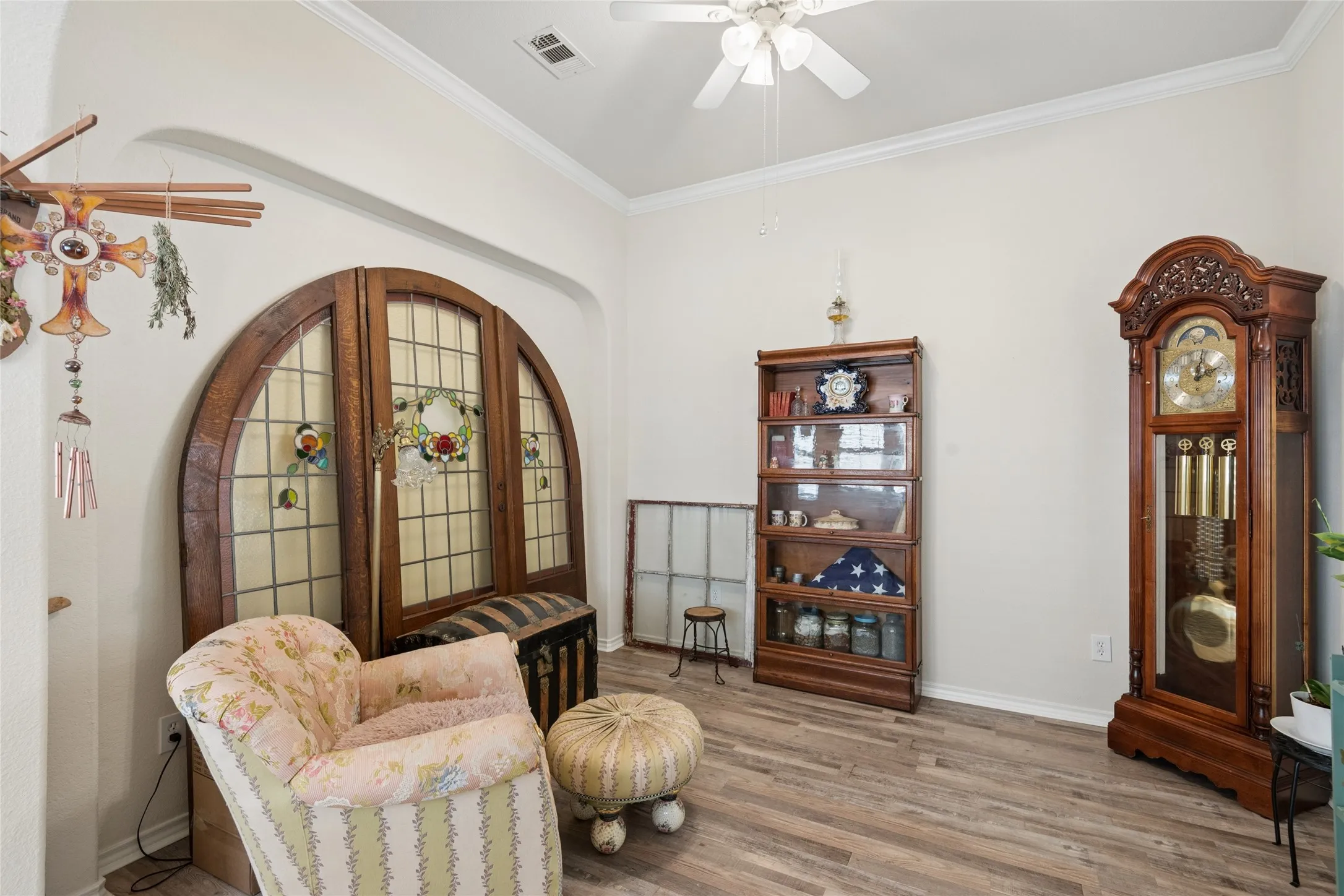 Wood-finish flooring, crown molding, arched wall opening, and a ceiling fan with light fixture