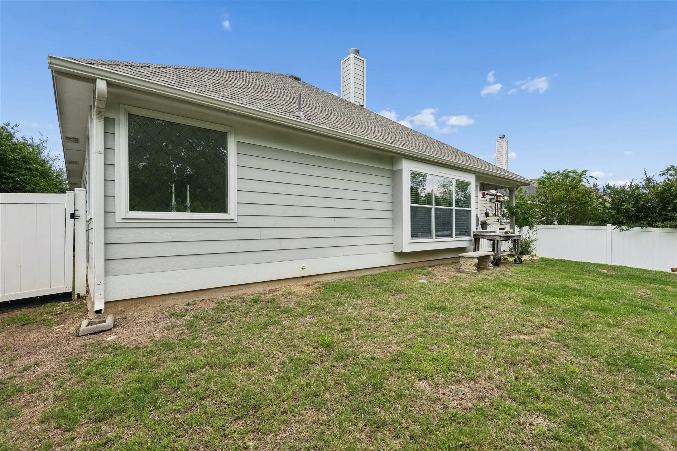 Bay window, white vinyl fencing, light gray siding, and a shingle roof