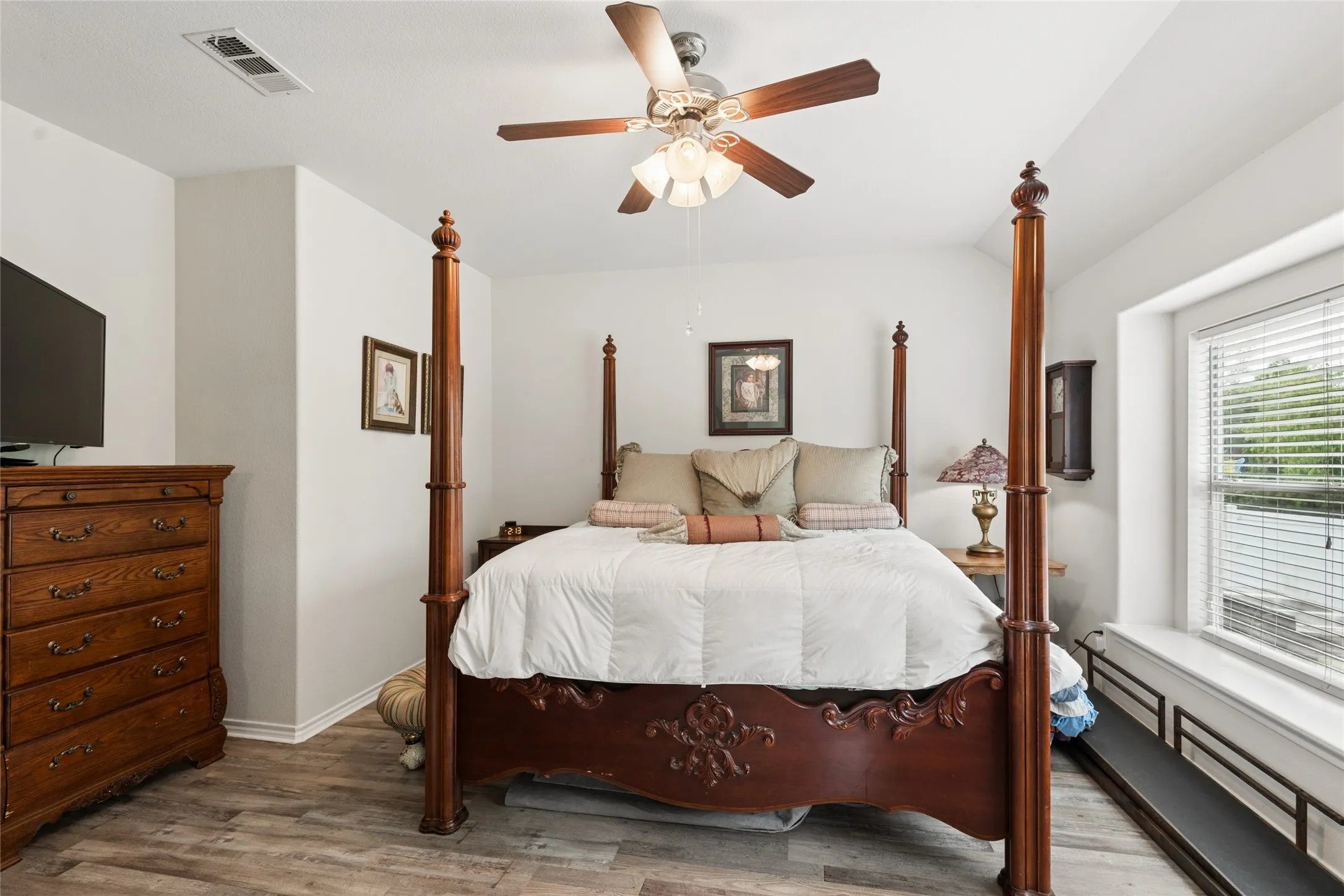 Wood-finish flooring, ceiling fan, white walls, and a window with blinds and a built-in window seat
