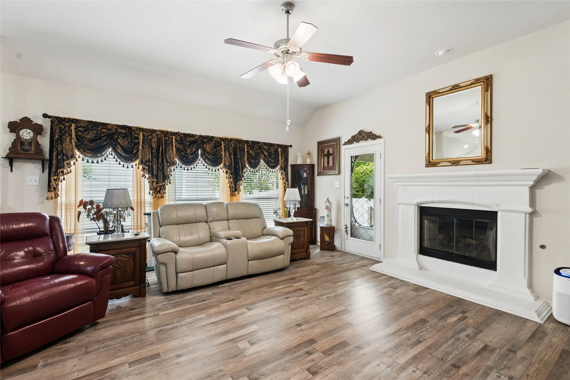 Wood-finish flooring, white fireplace with a mantel, white walls, ceiling fan with integrated lighting, and a glass-paneled door