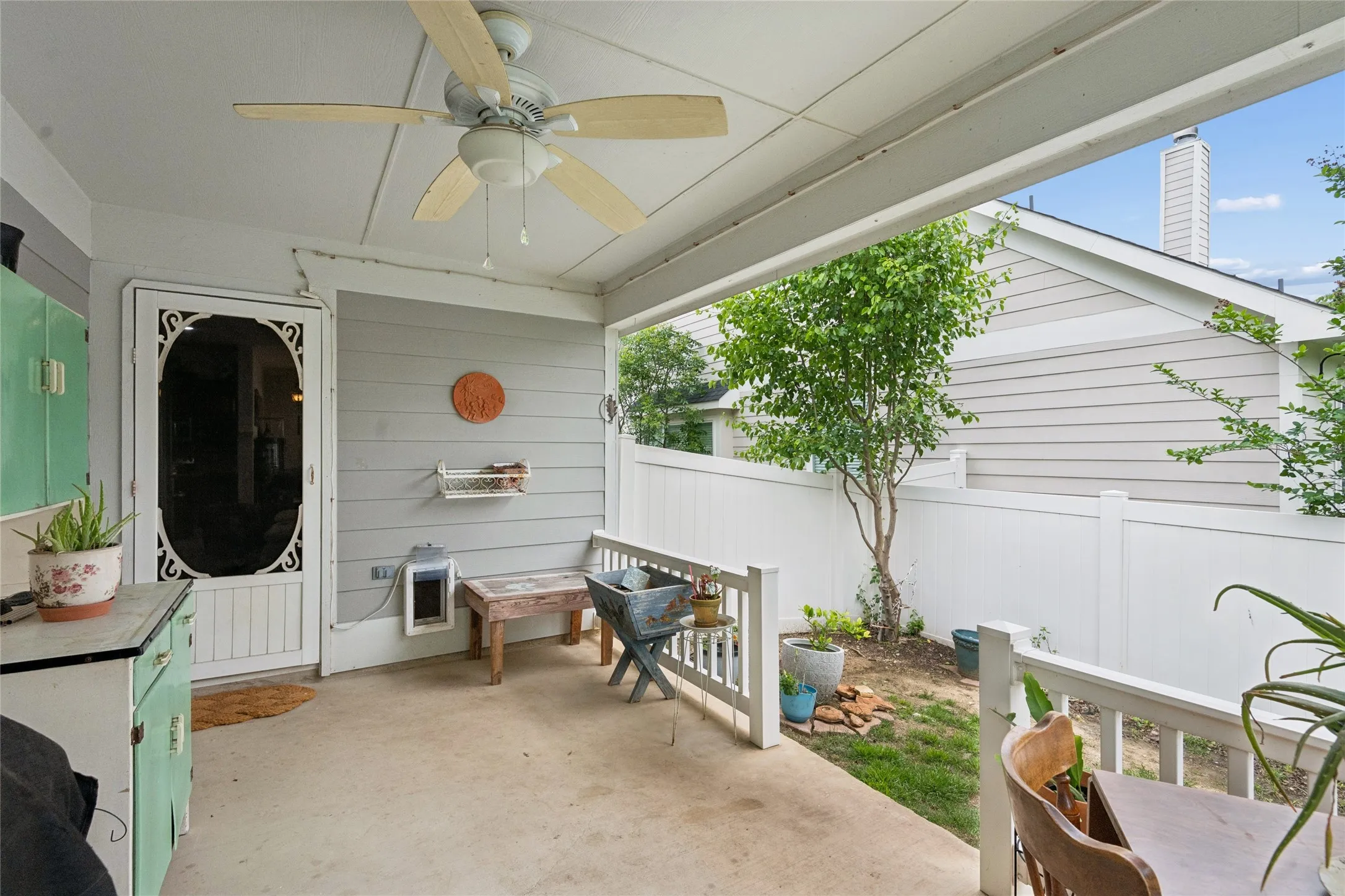 Covered patio with a ceiling fan, concrete flooring, and white privacy fencing