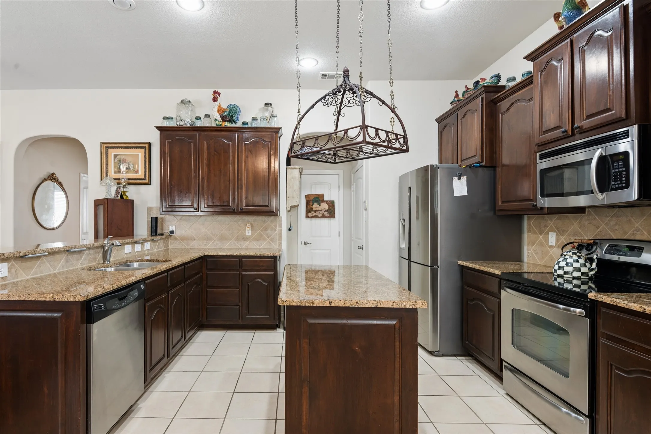 Kitchen featuring an island, wood cabinetry, granite countertops, tile flooring, and stainless steel appliances