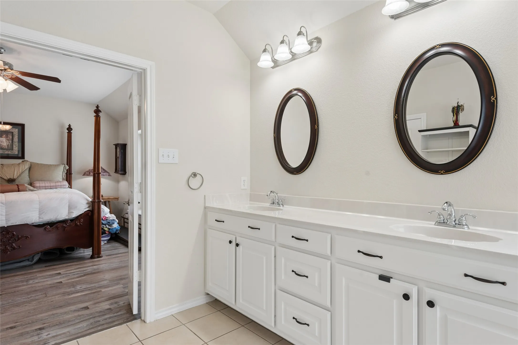 Dual vanity with integrated sinks and white cabinetry, featuring oval mirrors and overhead lighting
