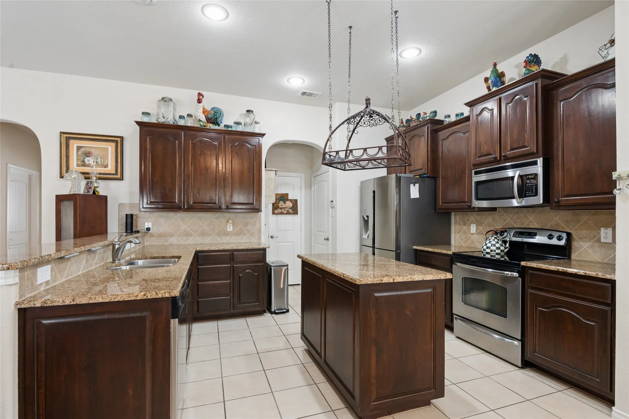 Kitchen featuring dark wood cabinetry, granite countertops, stainless steel appliances, a center island, and tiled flooring