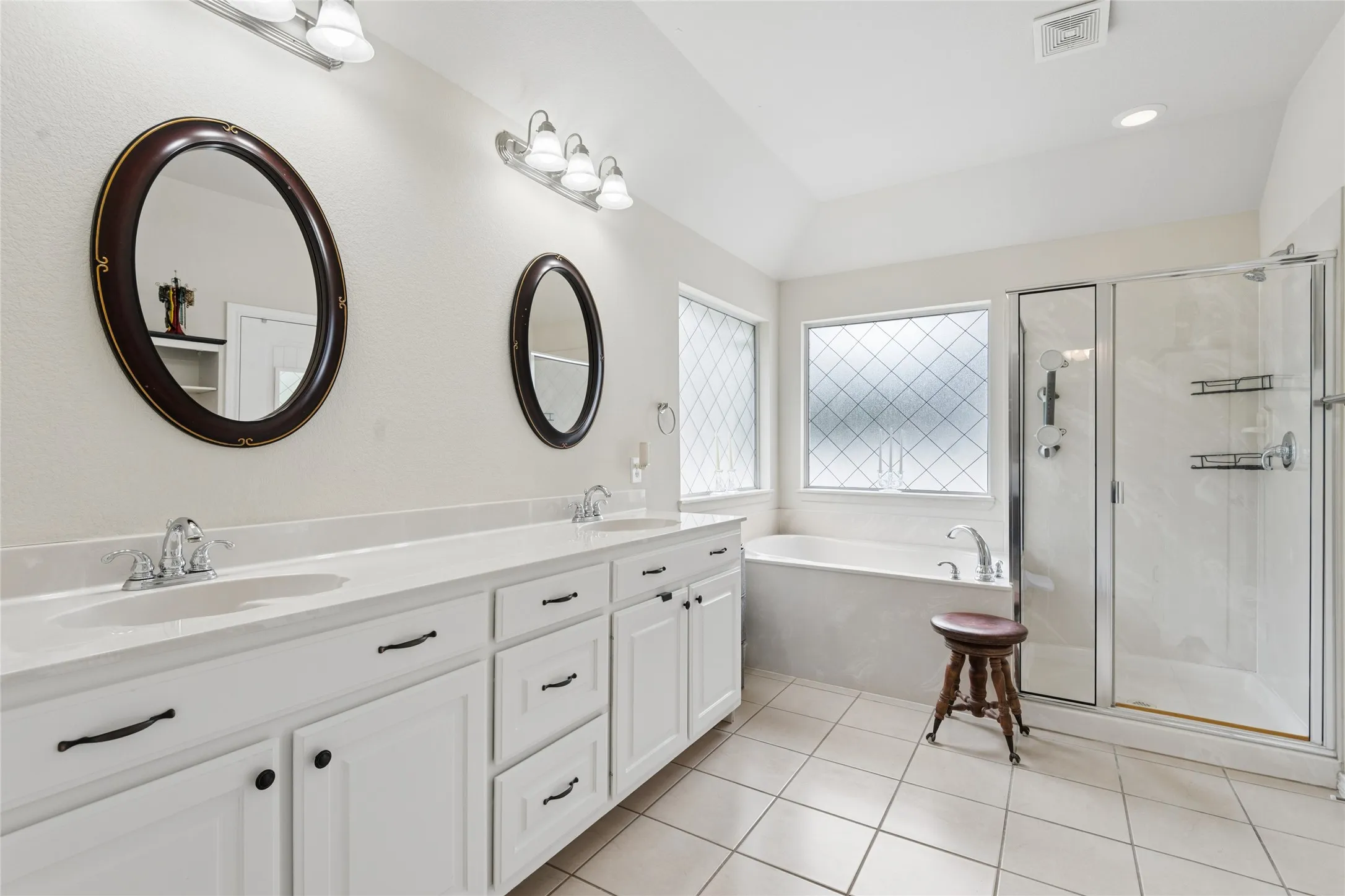 Dual vanity with white cabinetry and integrated sinks, a built-in bathtub, a separate glass-enclosed shower, and tiled flooring