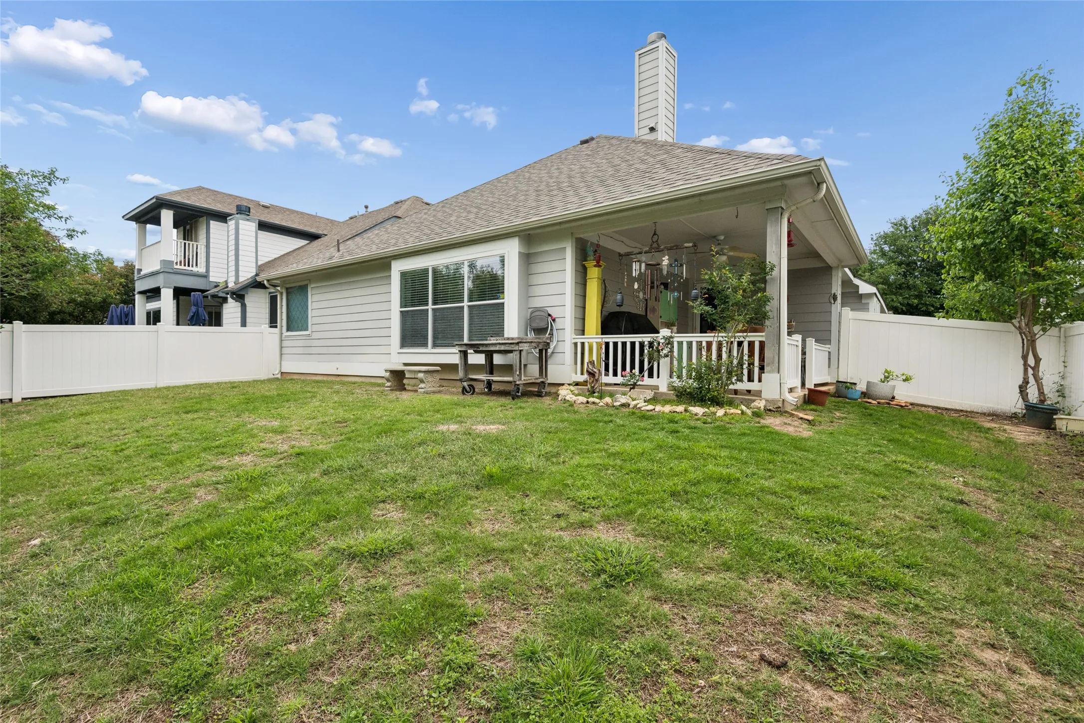 Expansive grassy backyard featuring a covered patio with white railing, vinyl fencing, and a side access gate