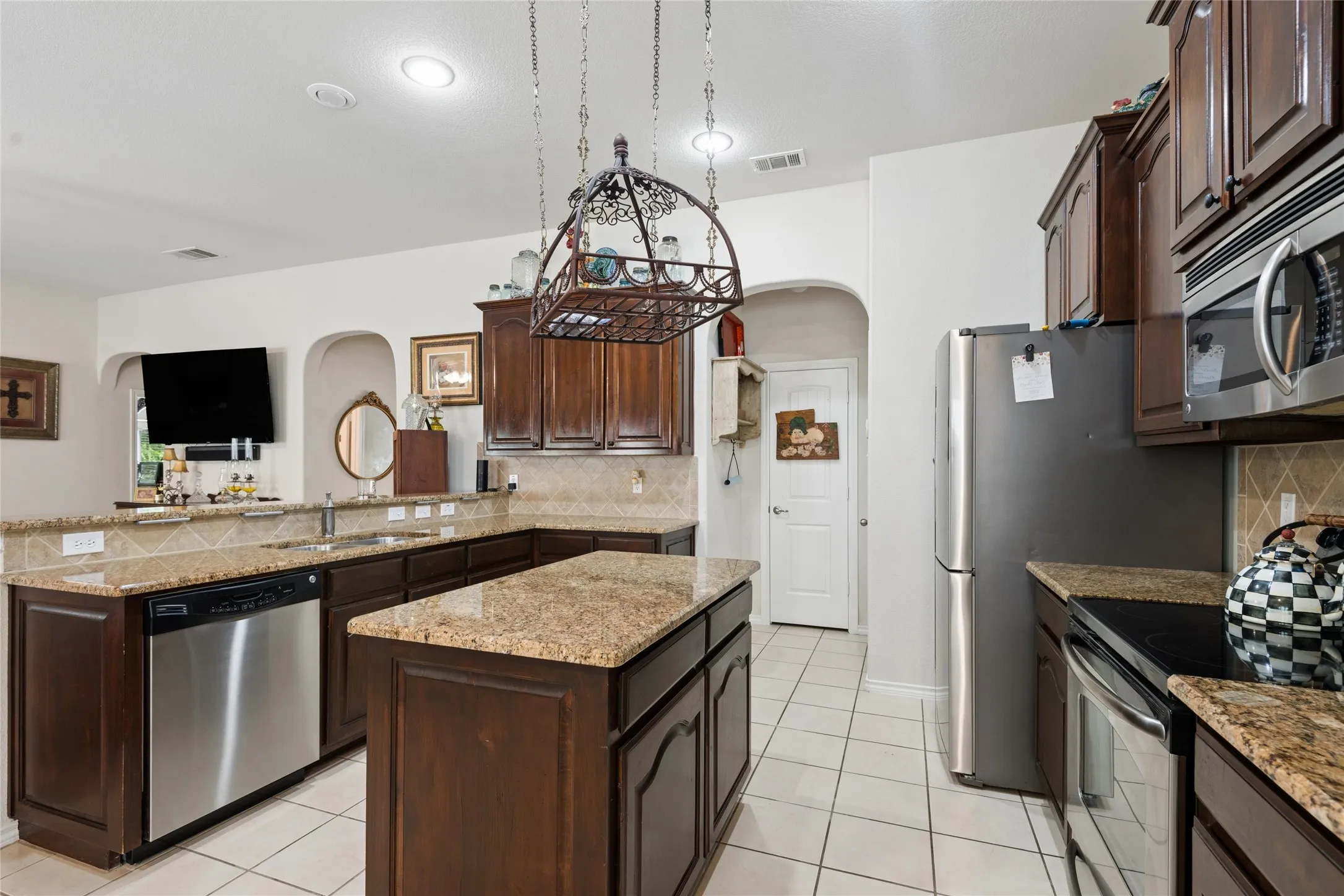 Kitchen featuring granite countertops, wood cabinetry, stainless steel appliances, a center island, and tile flooring
