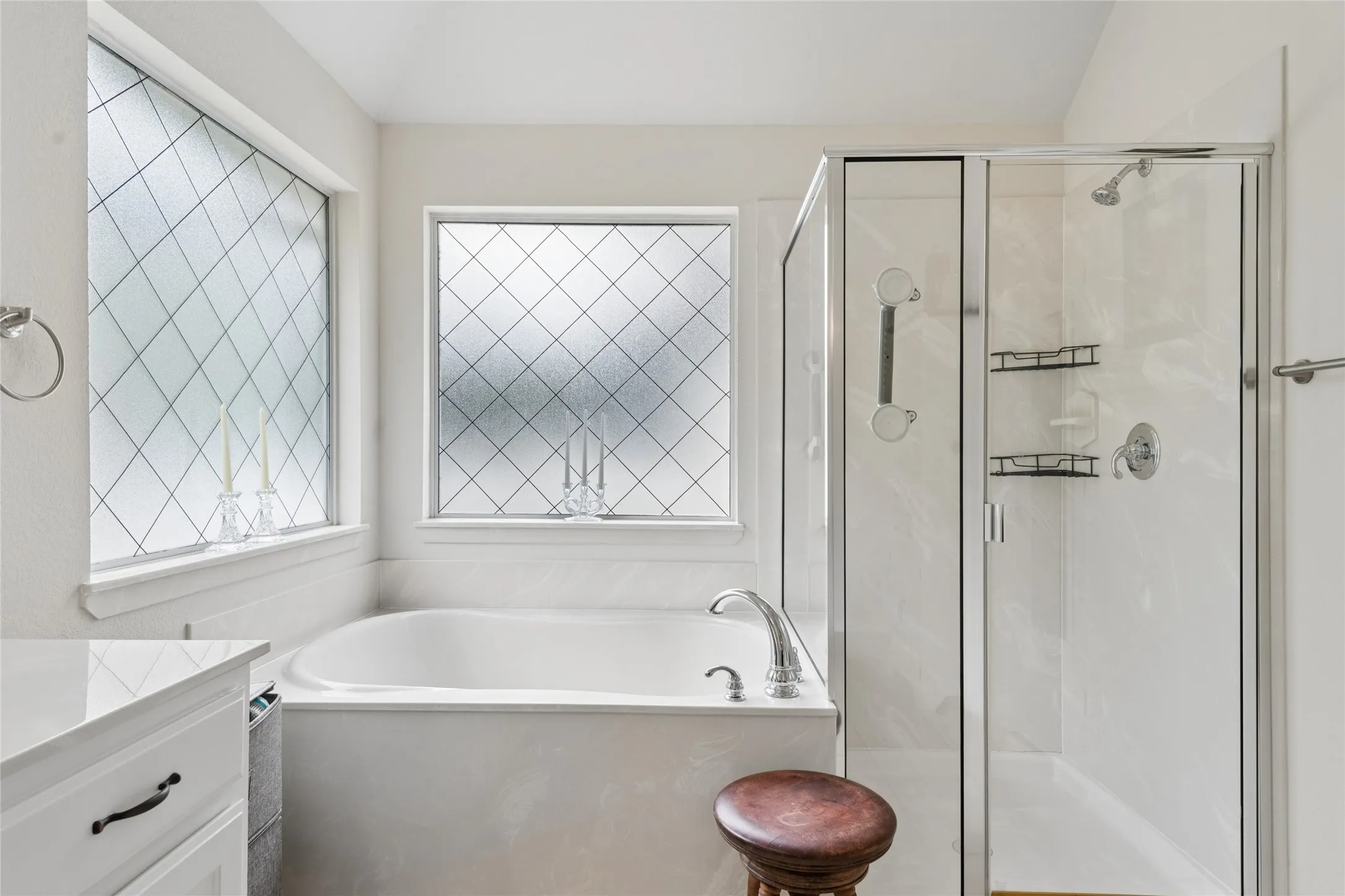 Built-in soaking tub with deck-mounted faucet, adjacent glass-enclosed shower with a rainfall showerhead, and a vanity with a white countertop