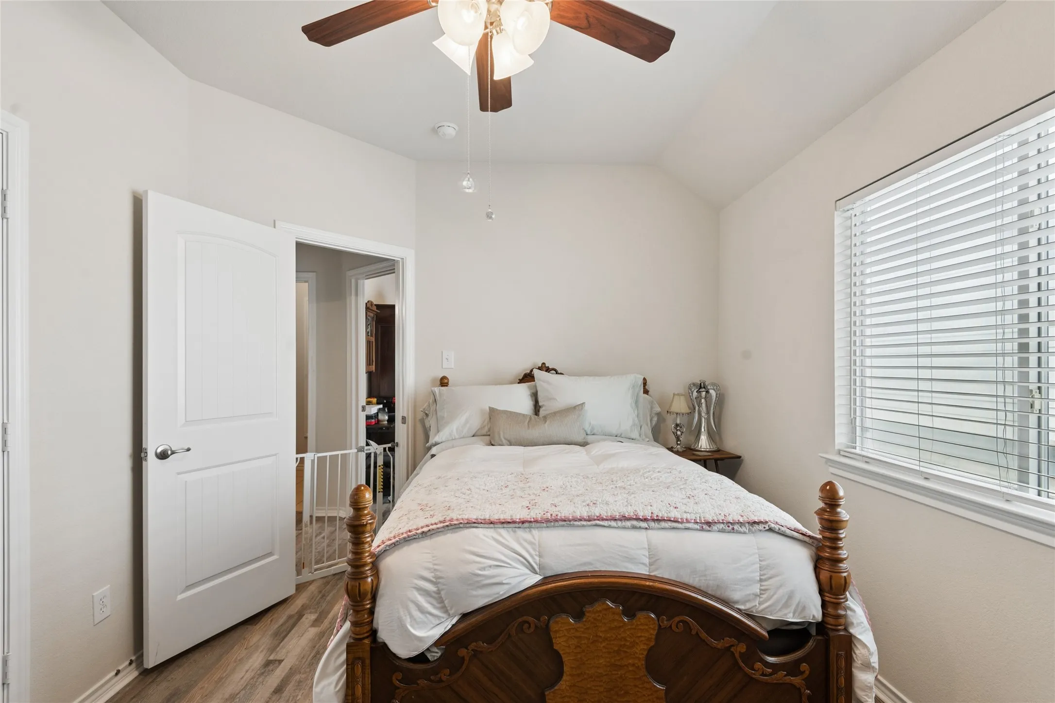 Vaulted ceiling with a ceiling fan light fixture, wood-finish flooring, and a window with blinds