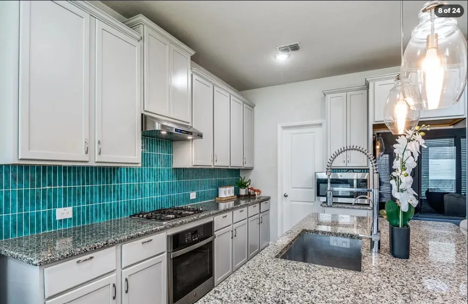 White cabinetry with crown molding, stainless steel appliances, granite countertops, a turquoise tile backsplash, and a large kitchen island with an undermount sink