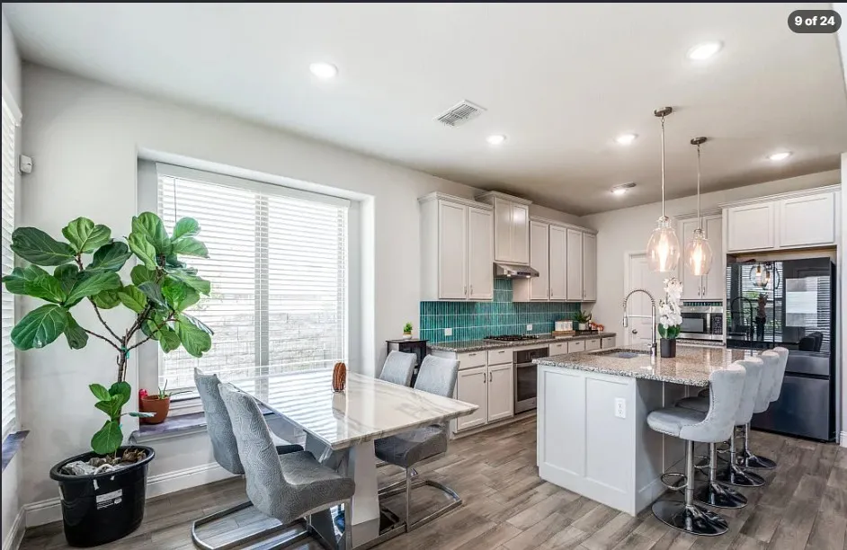 Kitchen featuring light-toned cabinetry, a spacious island with counter seating, stainless steel appliances, a unique tile backsplash, and wood-finish flooring