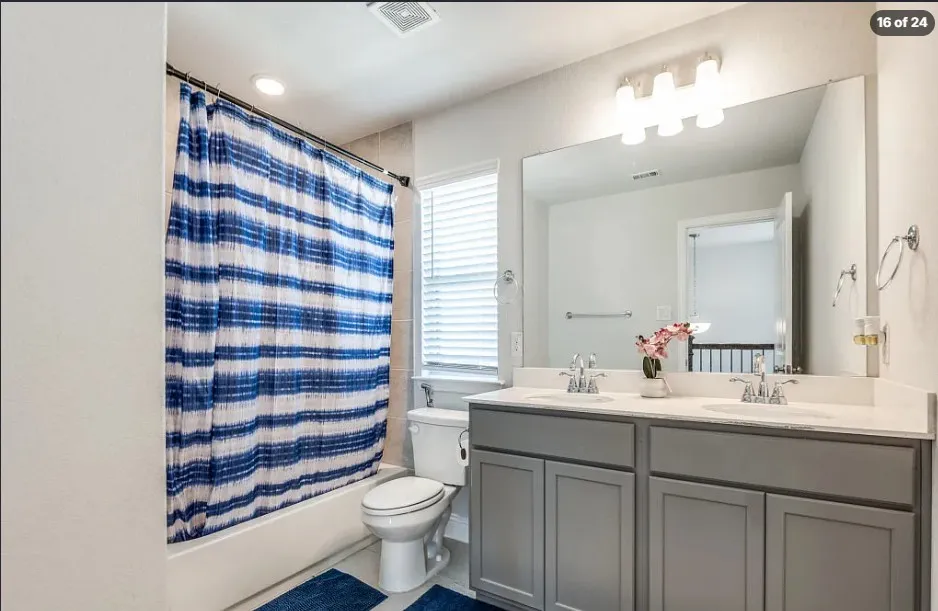 Dual vanity with undermount sinks and chrome fixtures, light-colored countertop, large wall-mounted mirror, recessed lighting, and a window with blinds