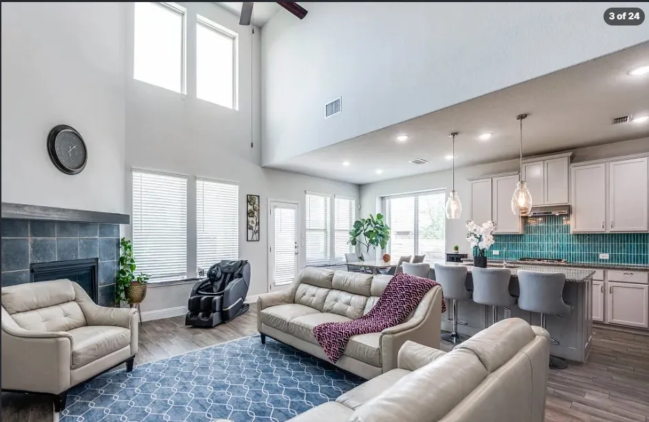 Vaulted ceiling with high windows, fireplace with tile surround, wood-finish flooring, kitchen island with seating, and subway tile backsplash