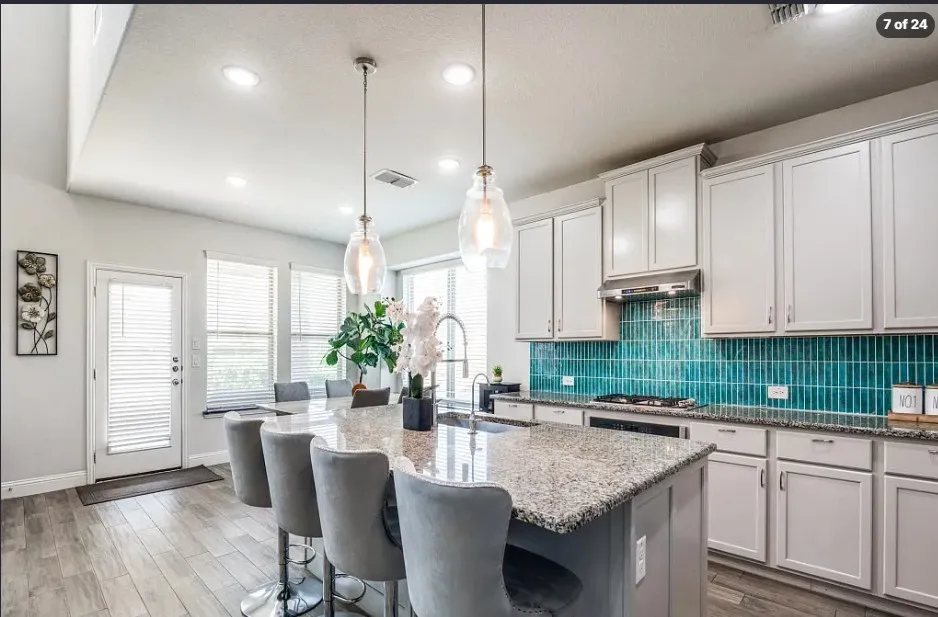 Kitchen featuring a granite island, pendant lighting, wood-finish flooring, white cabinetry, and a teal tile backsplash