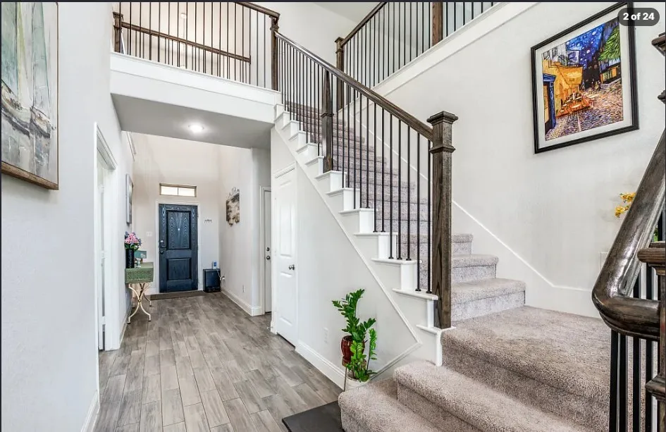 Two-story foyer featuring wood-finish flooring, a carpeted staircase with dark wood newel posts, and a black wrought iron baluster system