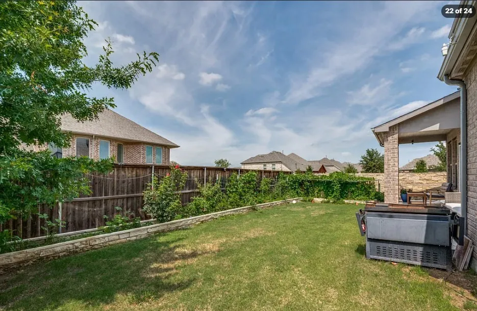 Expansive backyard featuring a manicured lawn, wood fencing, and a stone retaining wall